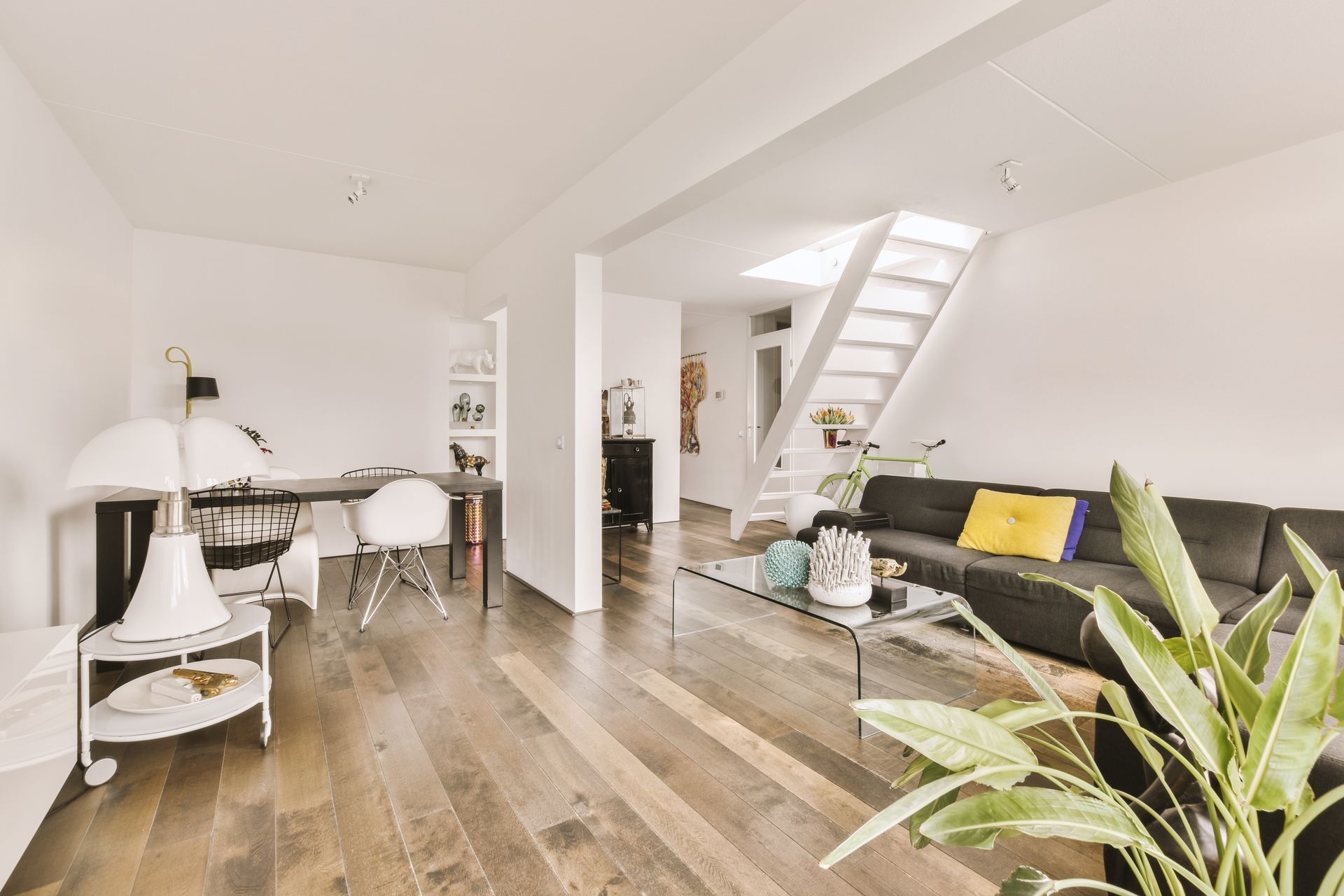 Modern living room with dark wood floors, black sofa, and a staircase.