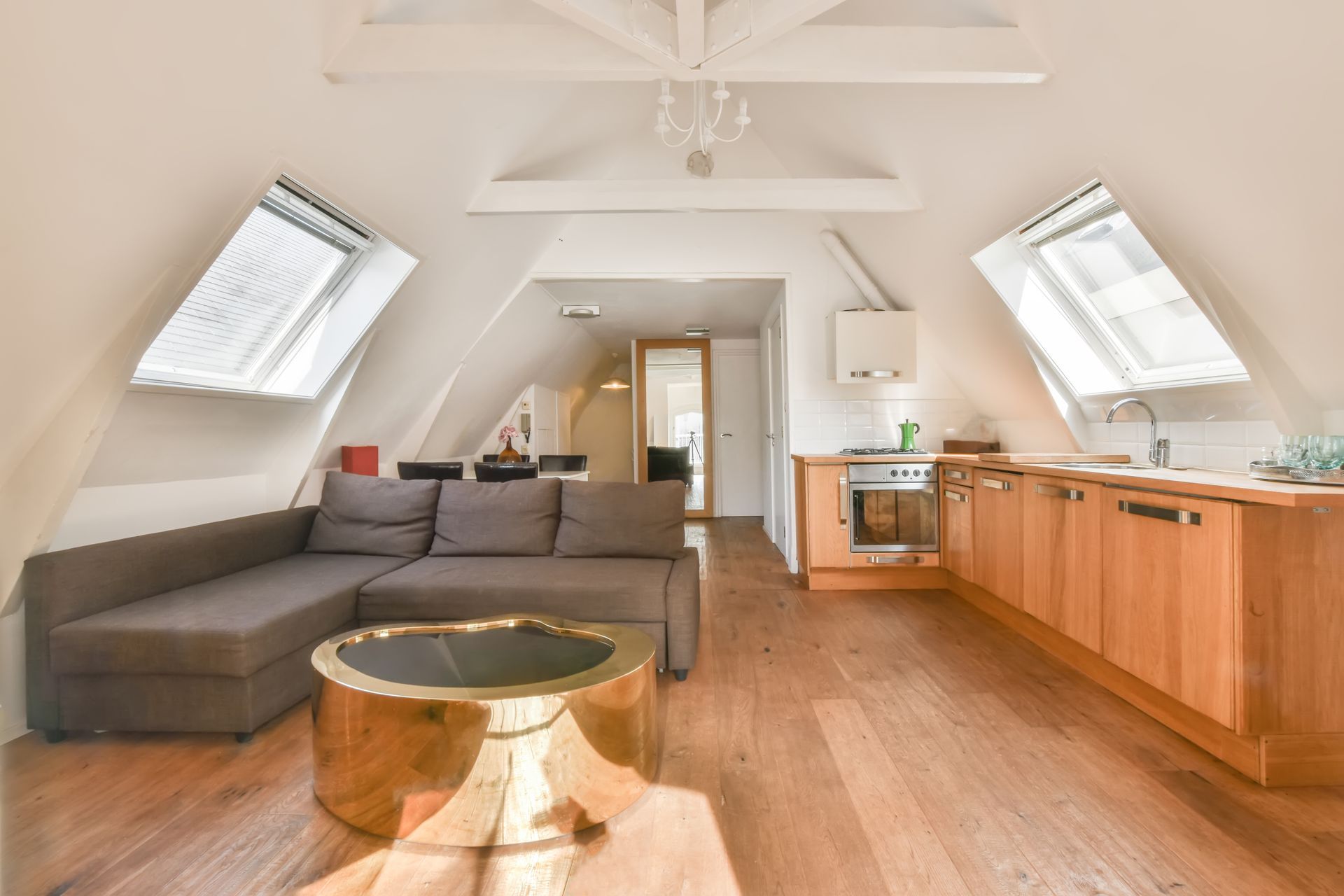 Living space with wood floors, gray couch, light wood kitchen, and angled skylights.