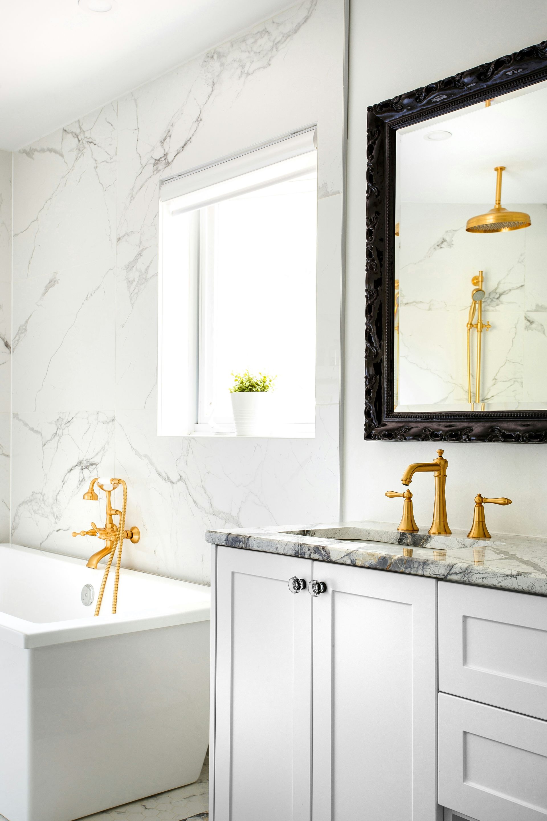 Elegant white bathroom with marble walls, gold fixtures, and black-framed mirror.