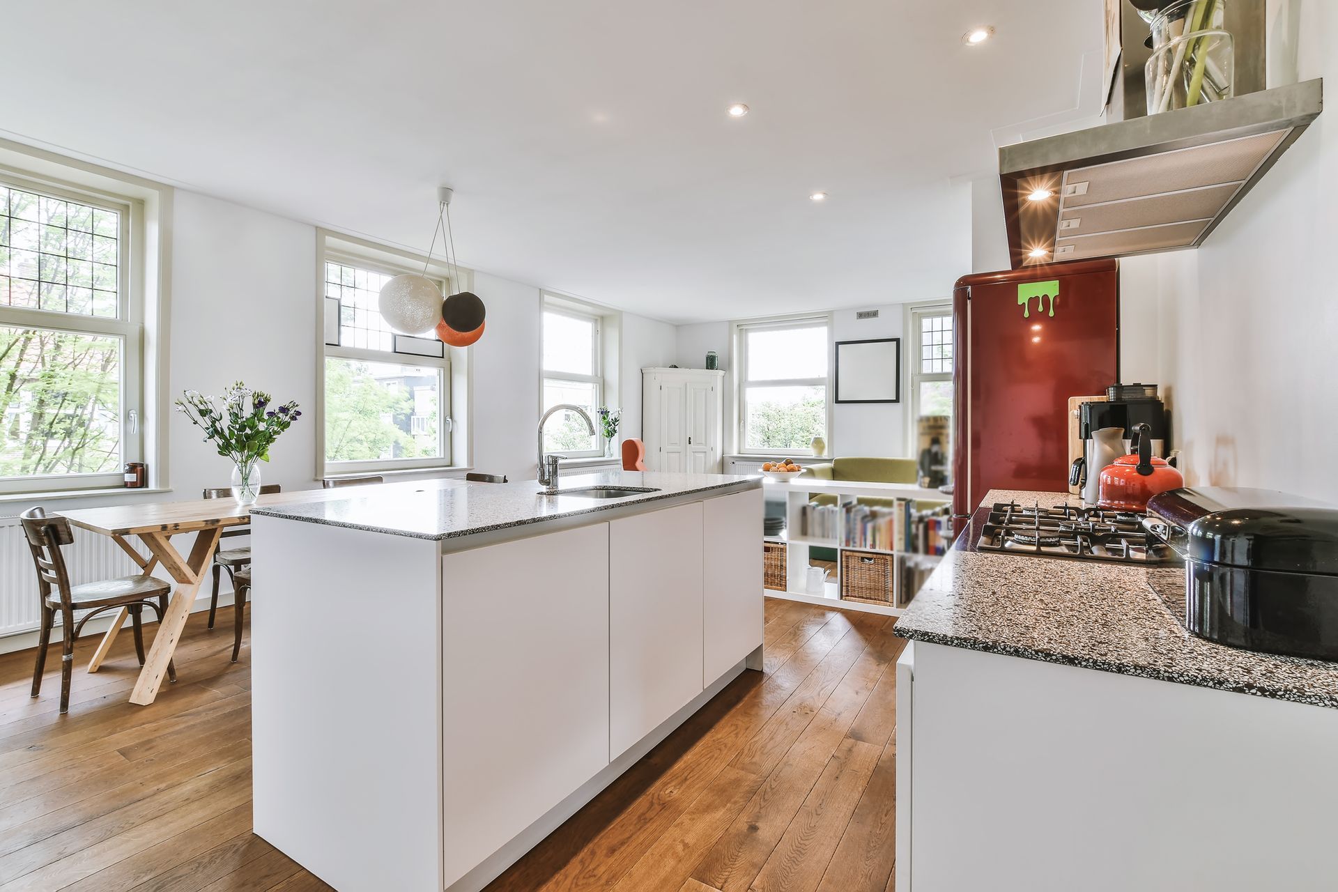 Modern kitchen with white island, red fridge, dining table, and windows.