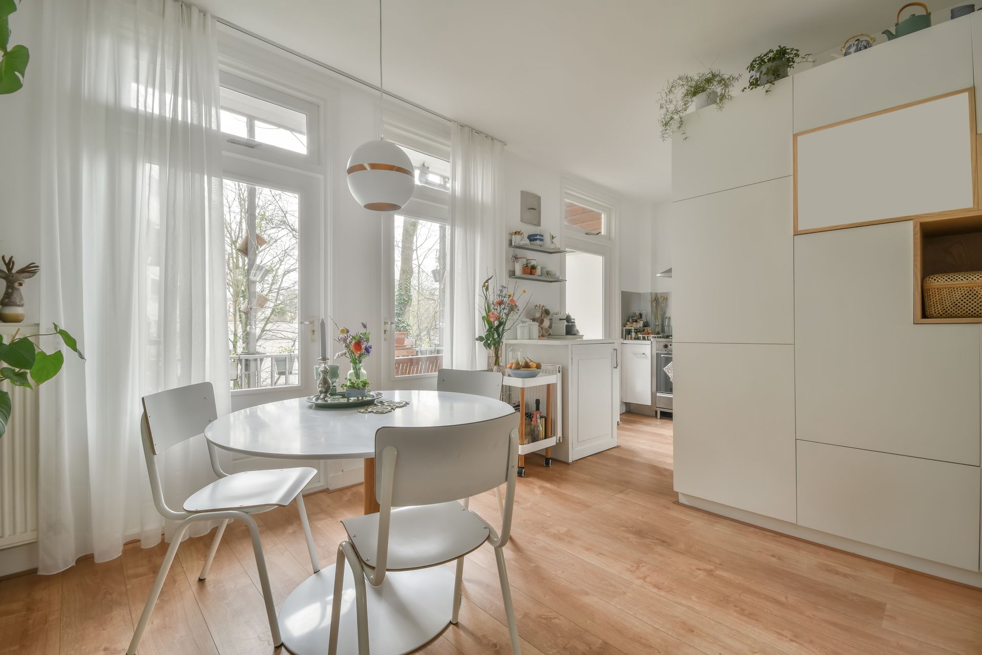 Bright dining room with a round white table, white chairs, and sheer curtains.