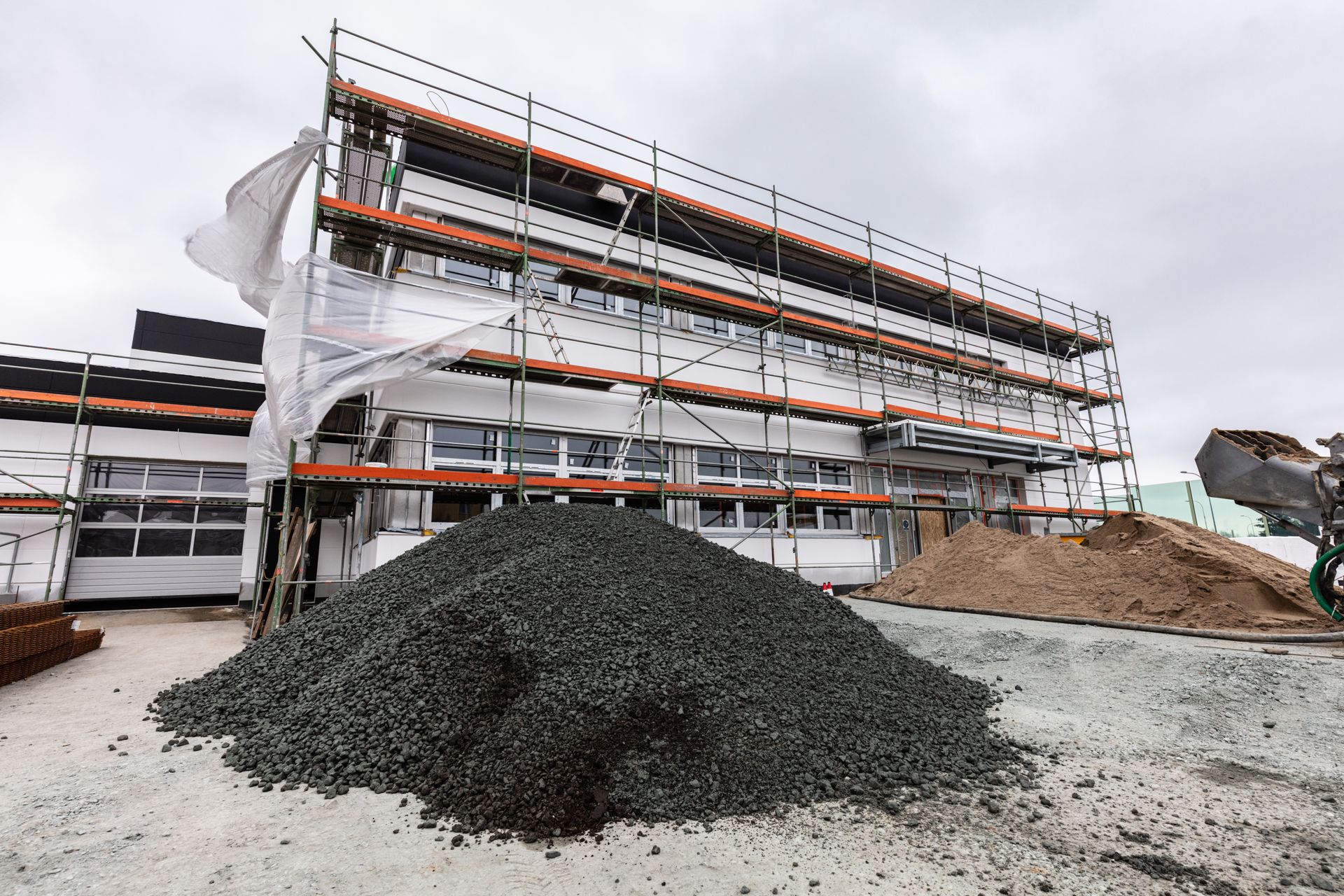 Building under construction with scaffolding, piles of gravel, and cloudy sky.