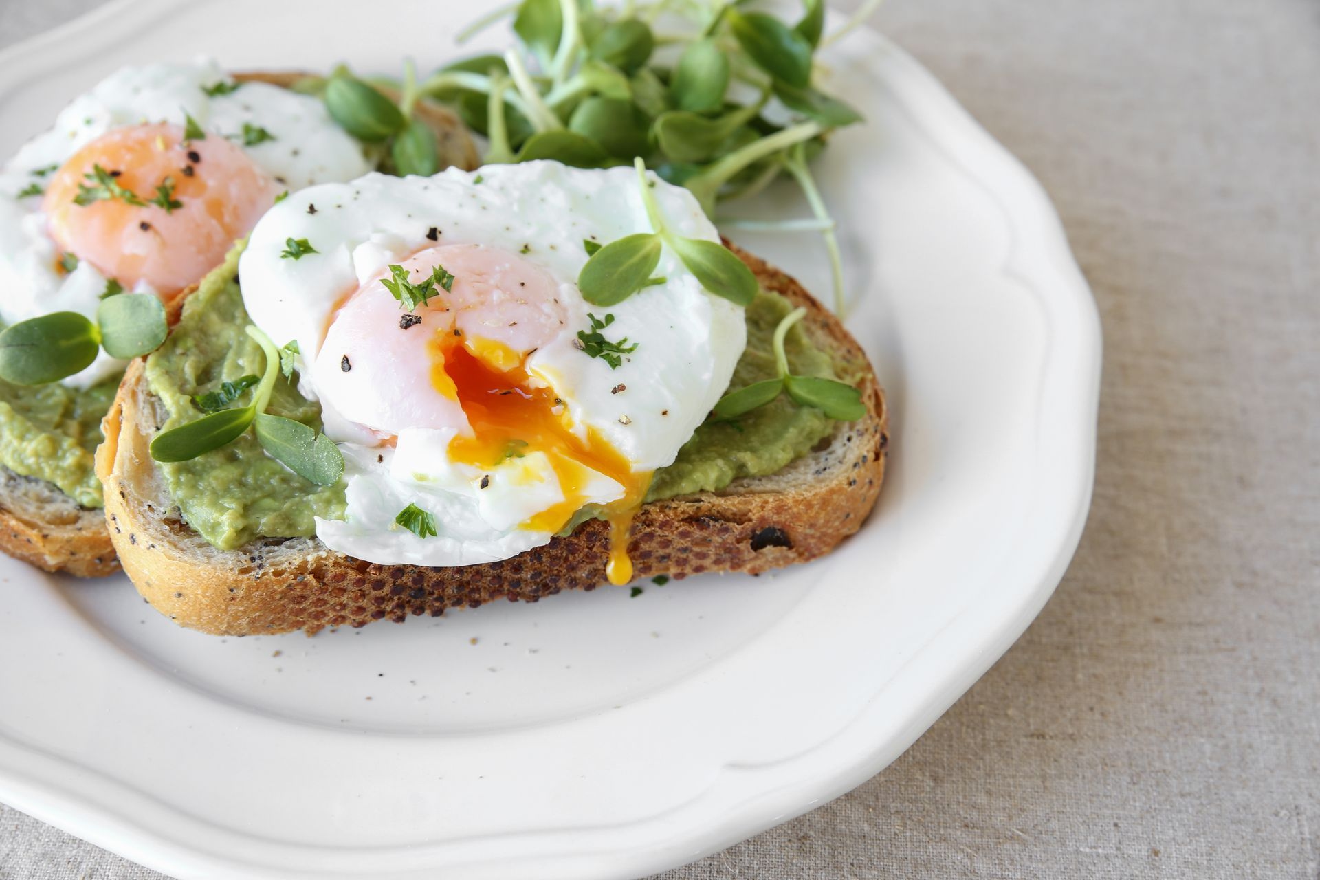 Two slices of avocado toast with poached eggs on a white plate