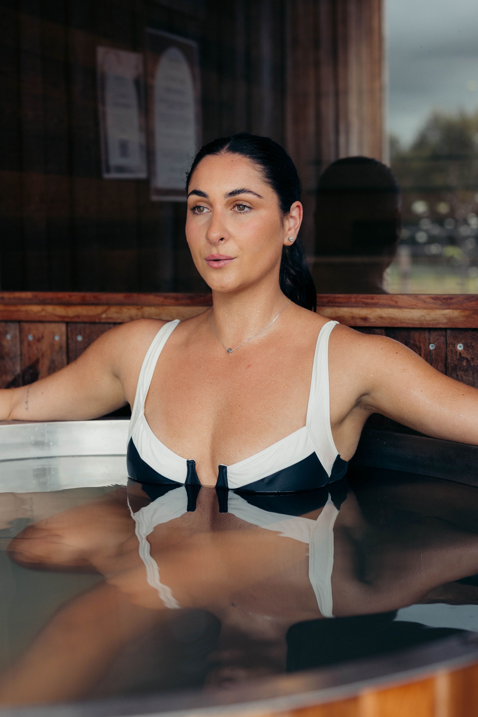 Woman in a swimsuit relaxing in a spa, arms open, looking forward.