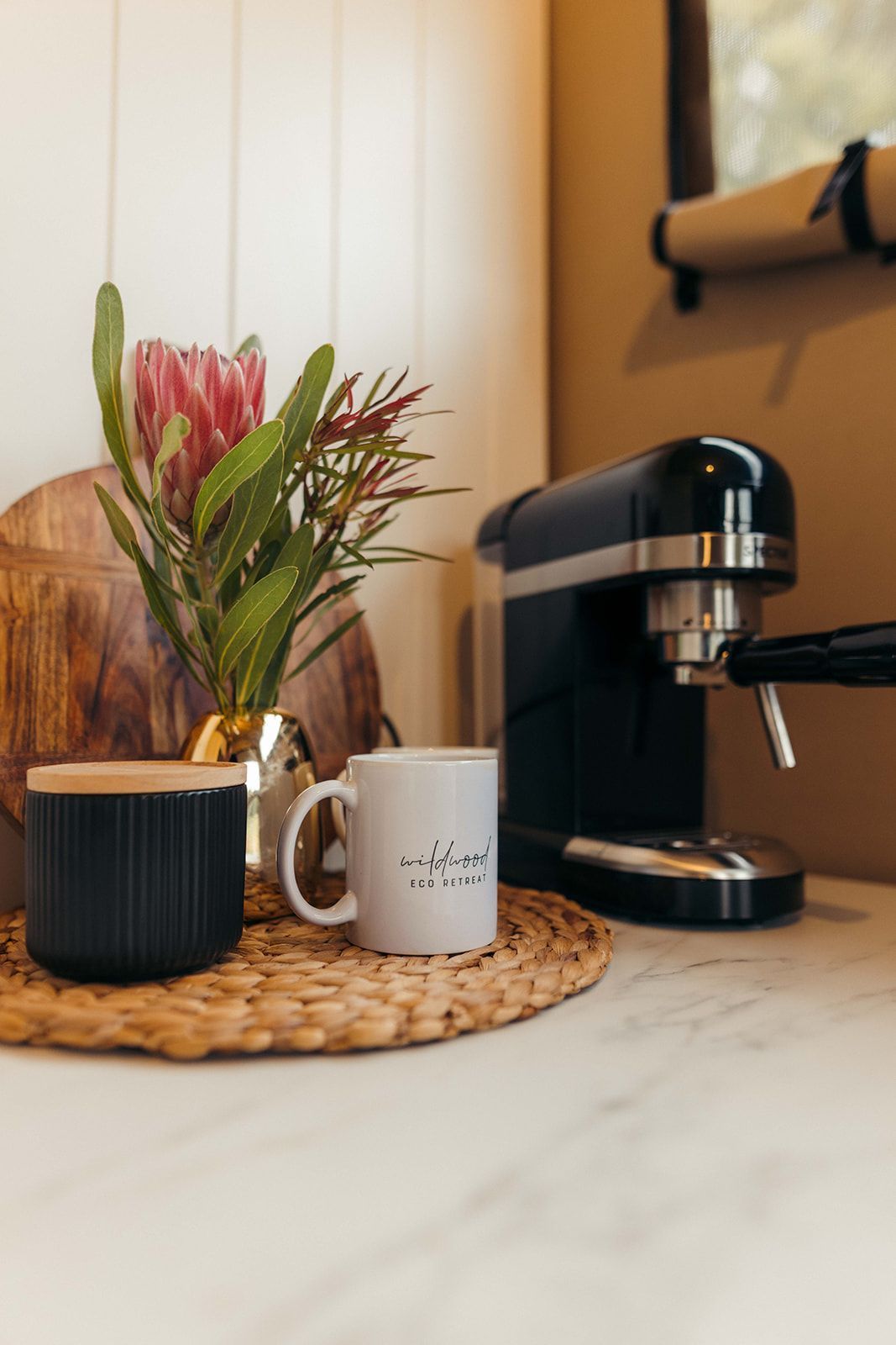 Coffee station with espresso machine, mug, floral arrangement, and black candle on countertop.