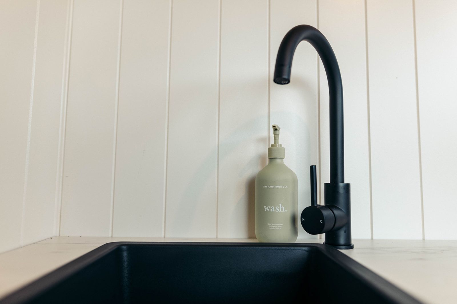 Black faucet over a black sink with a soap dispenser against white paneled wall.