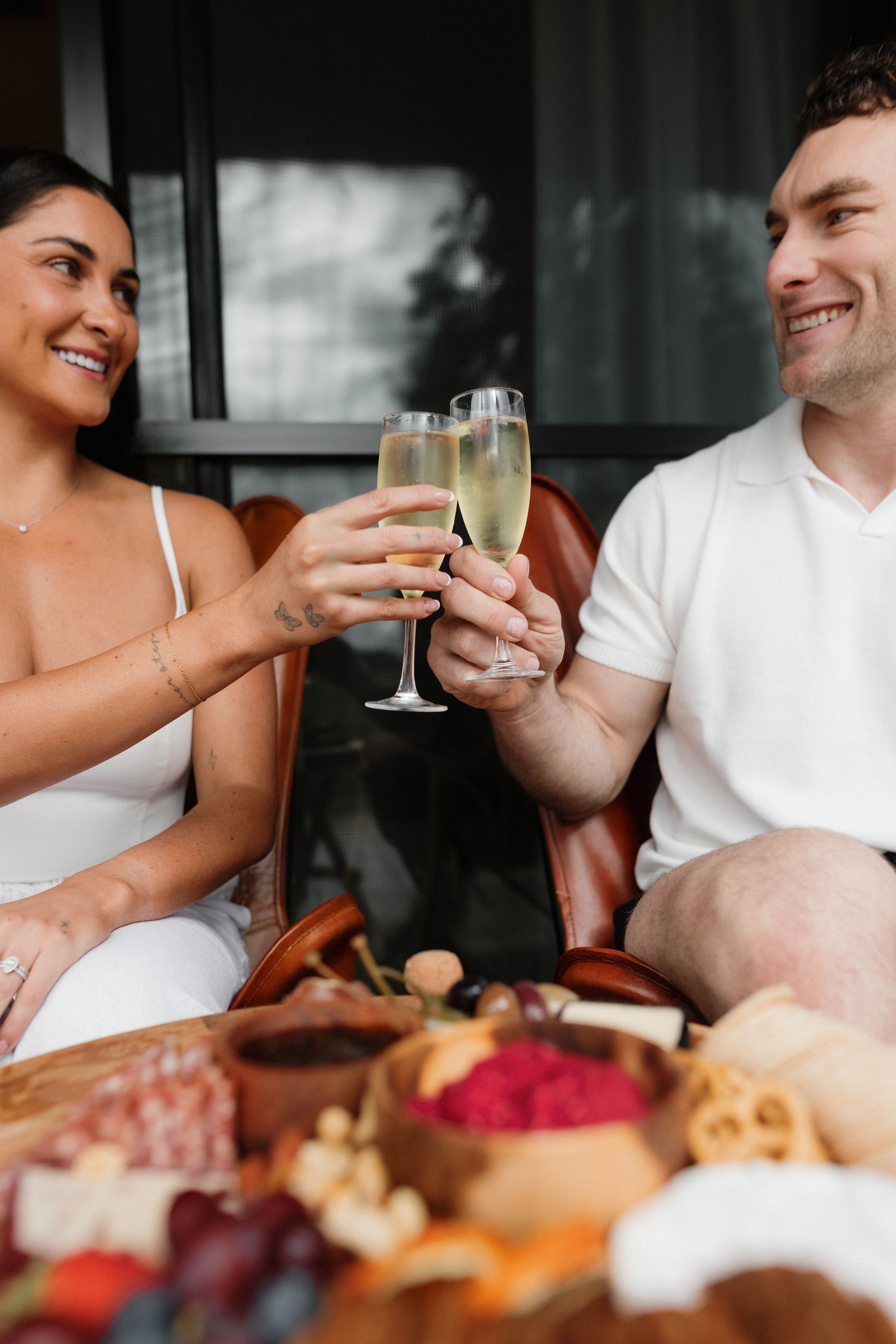 Couple toasting with champagne, smiling at a charcuterie board.