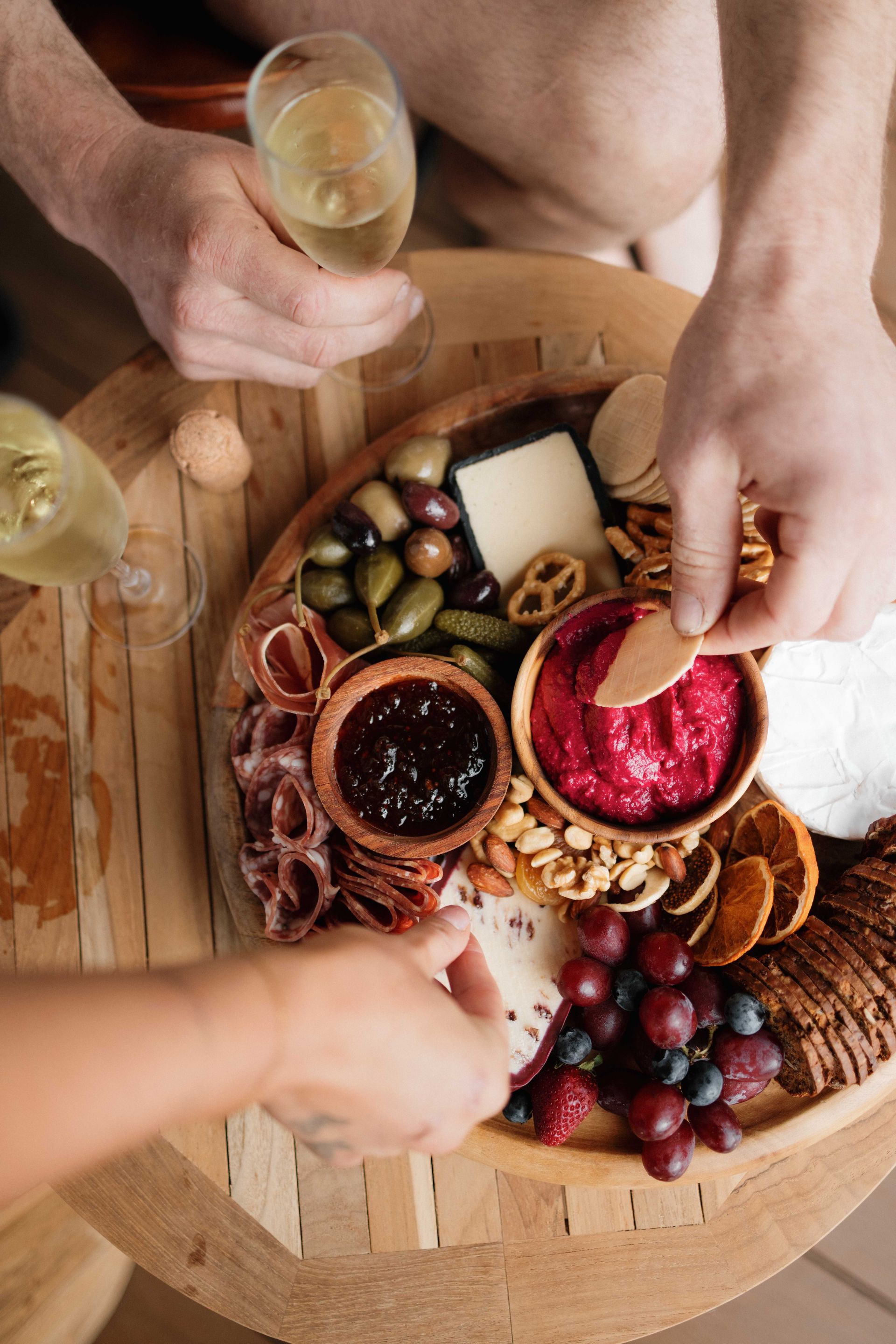 Charcuterie board with hands reaching for food, glasses of white wine.