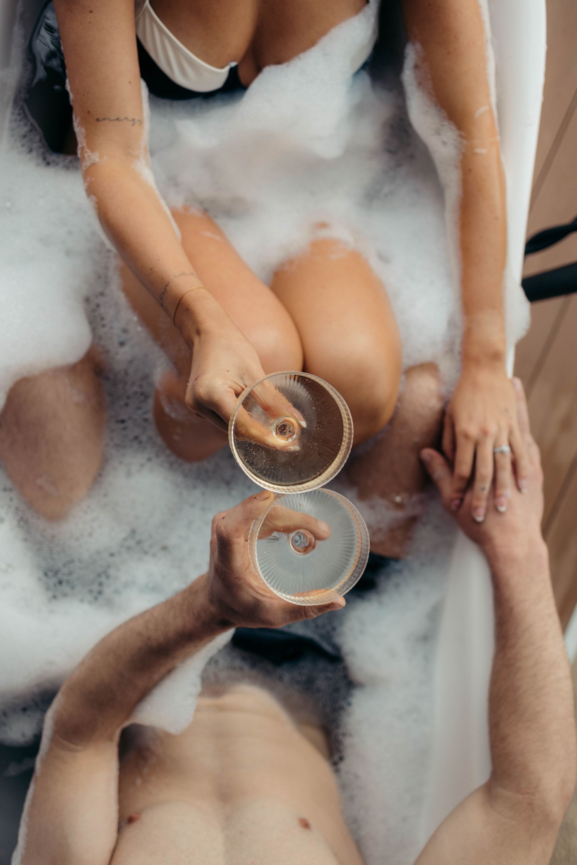 Couple in a bubble bath, toasting with champagne glasses.