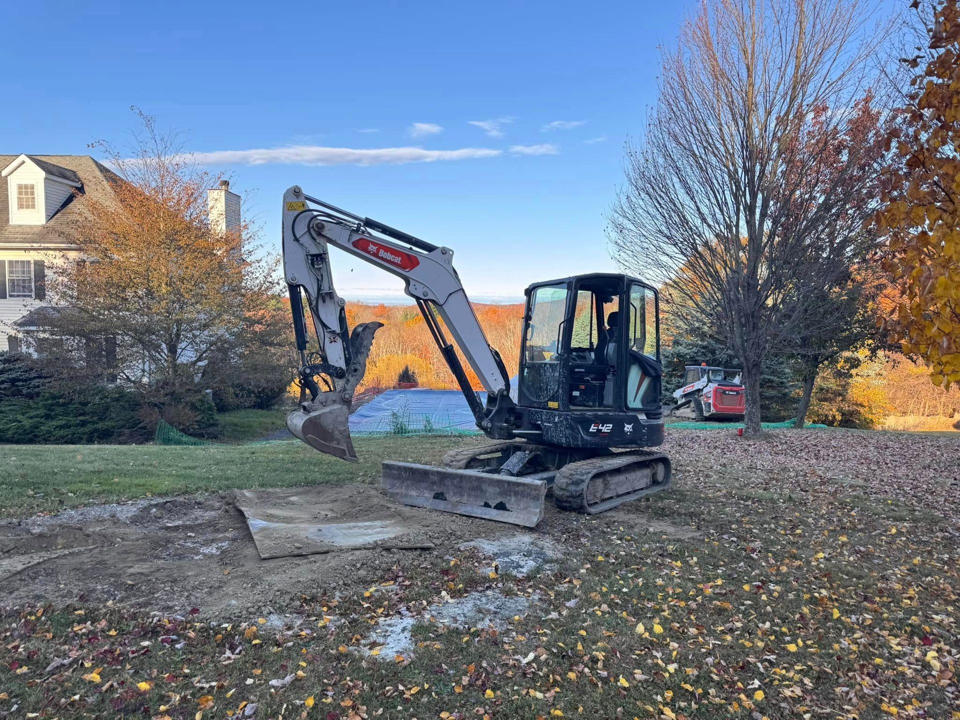 A small excavator is sitting in a yard next to a house.