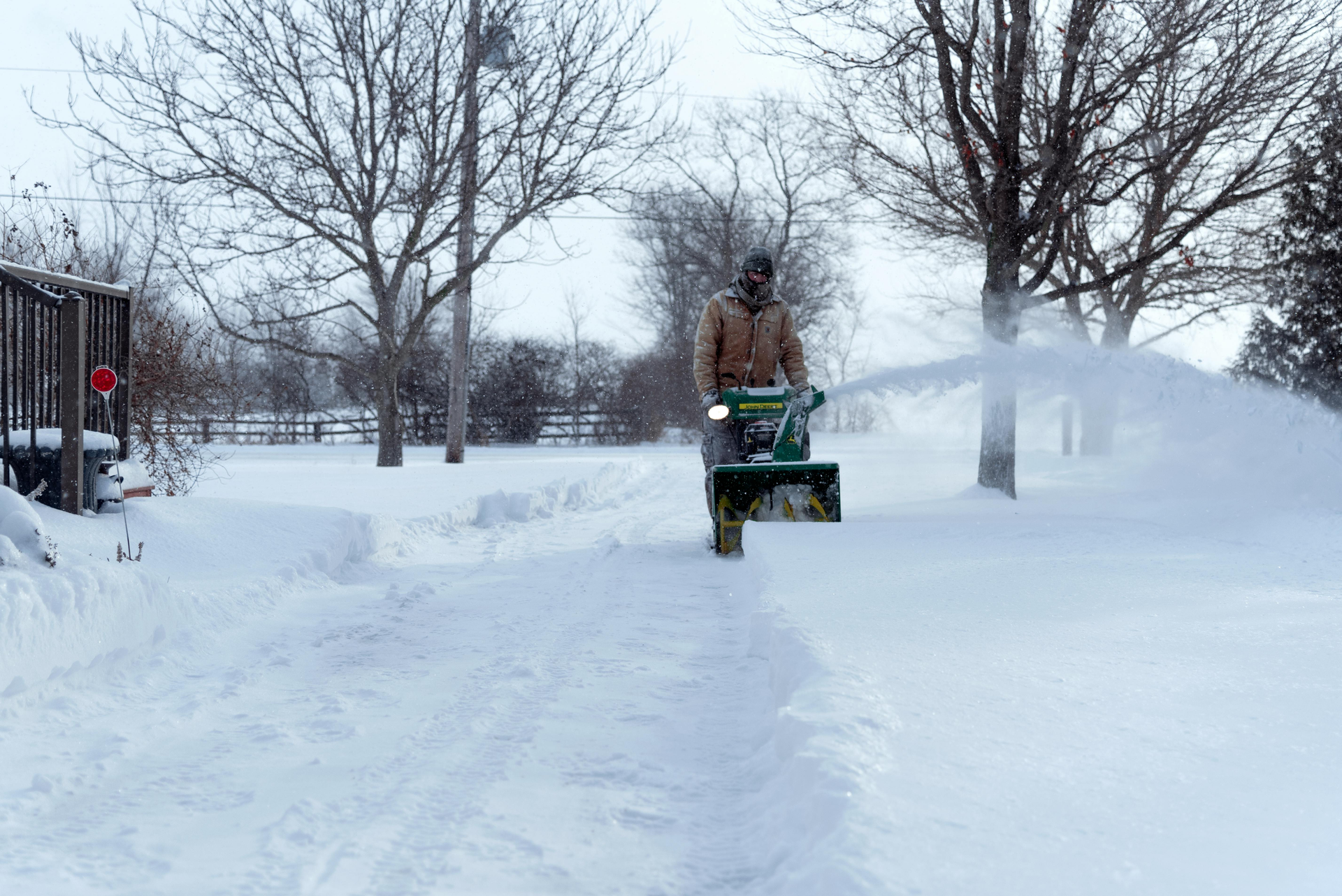 A man is using a snow blower to clear a snowy driveway.