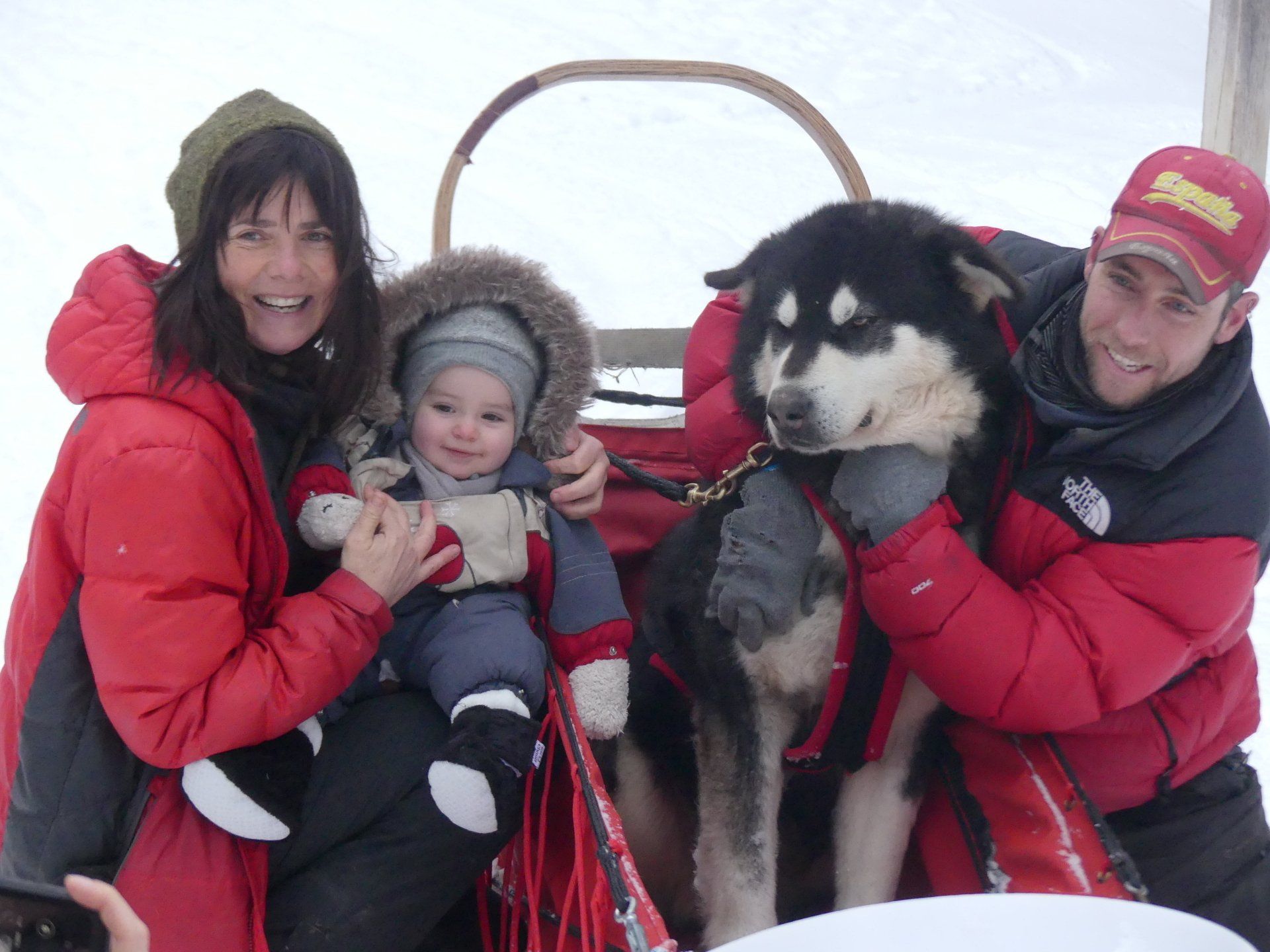 Un homme portant une veste North Face tient un bébé et un chien