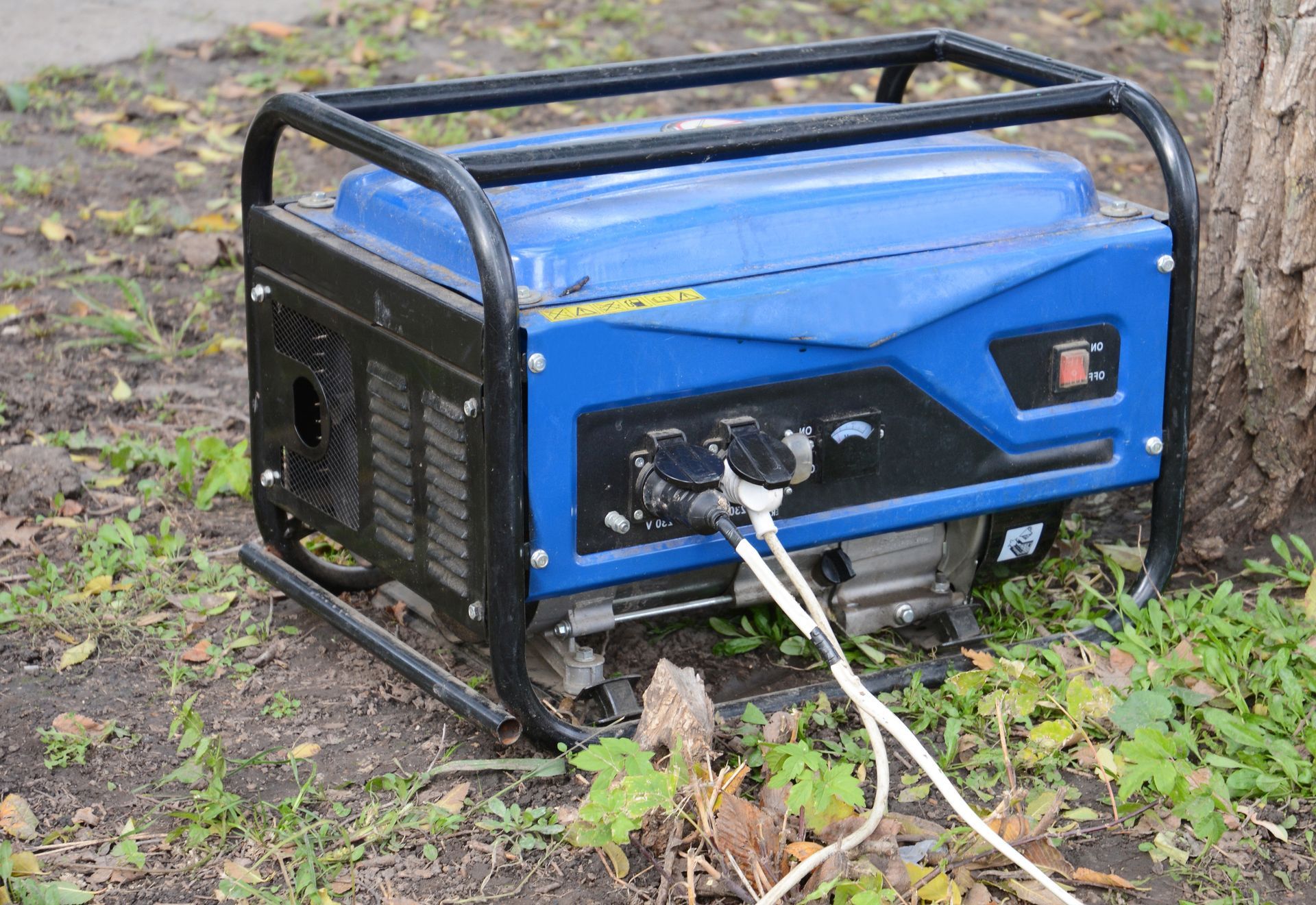 A blue generator is sitting in the grass next to a tree.