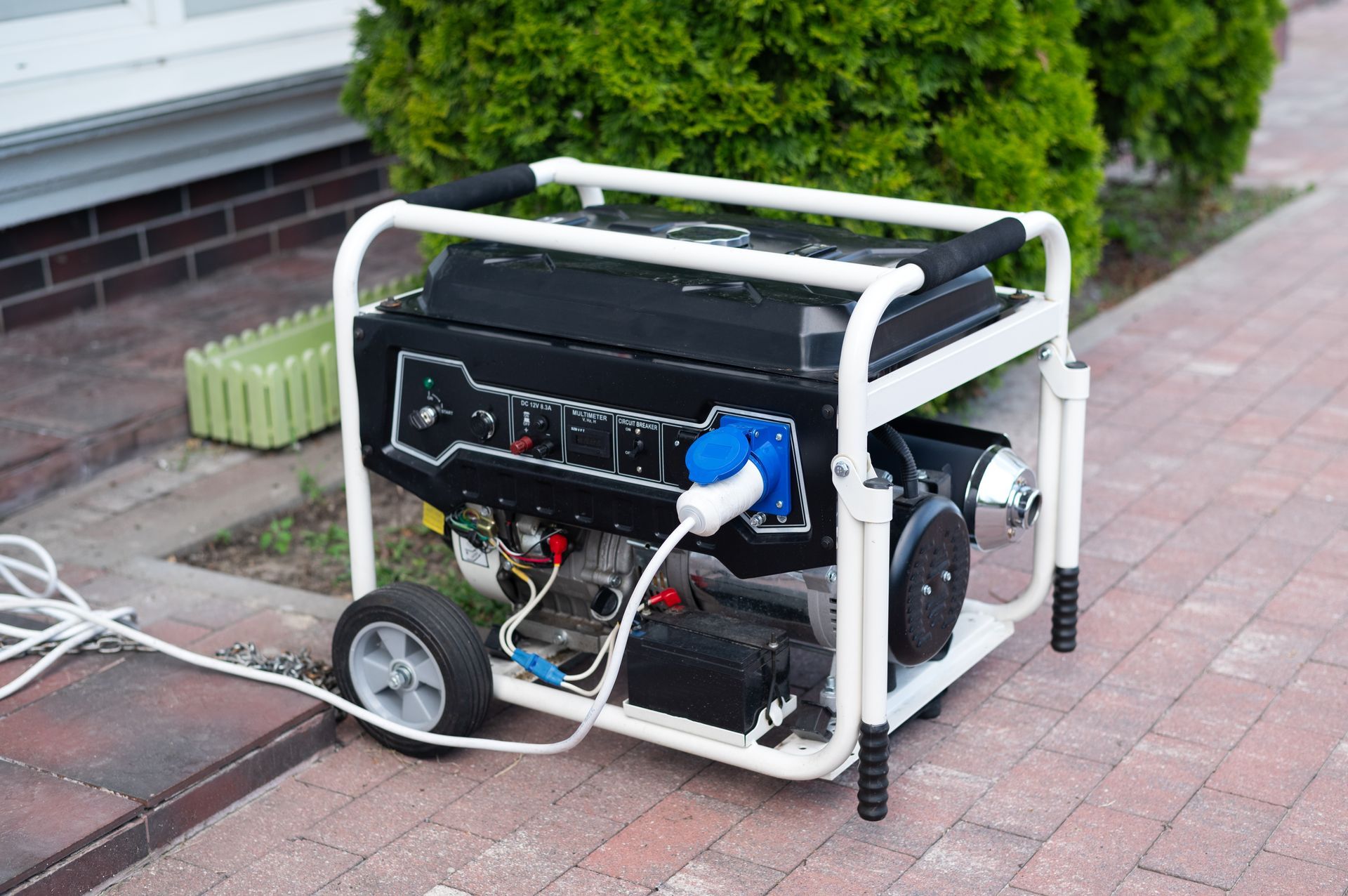 A generator is sitting on a brick sidewalk next to a bush.