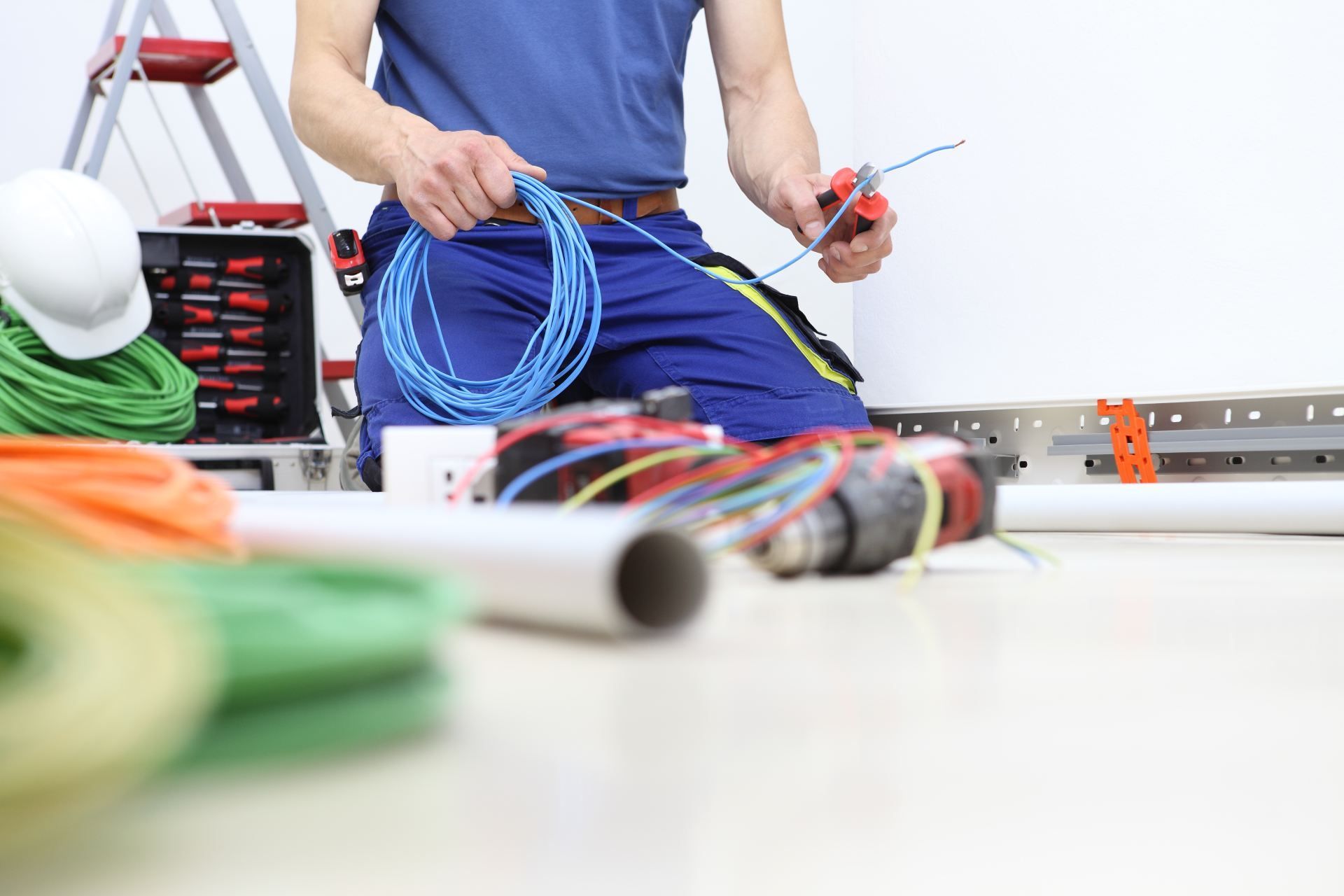 Electrician kneeling, working with blue wires, surrounded by tools and cables.