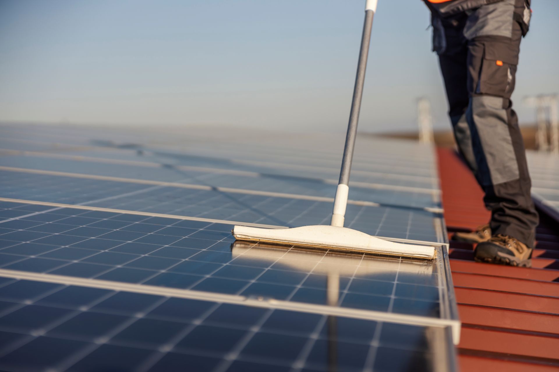 Person cleaning solar panels with a squeegee on a rooftop.