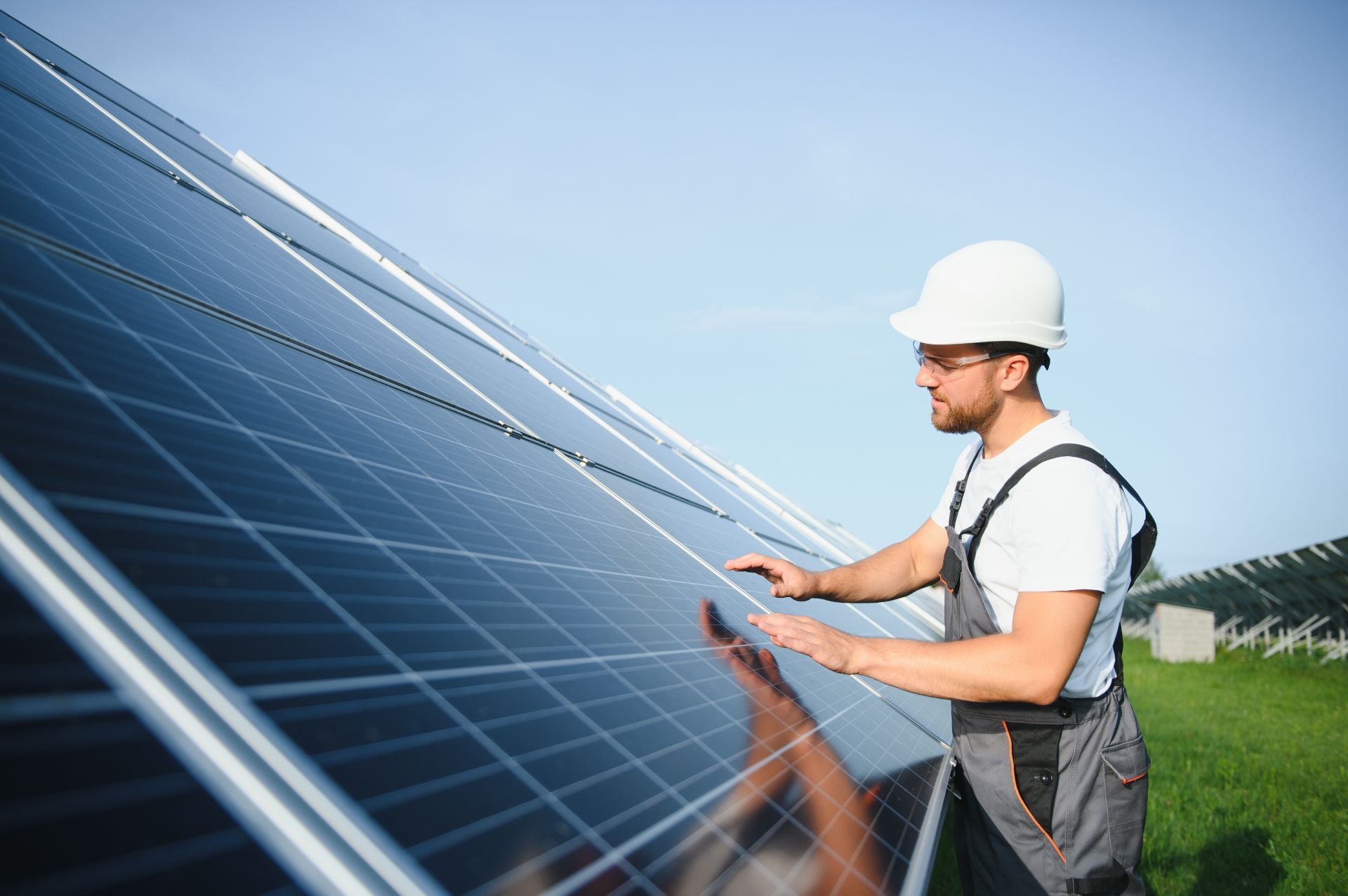 Man in hard hat inspects solar panels in a field.