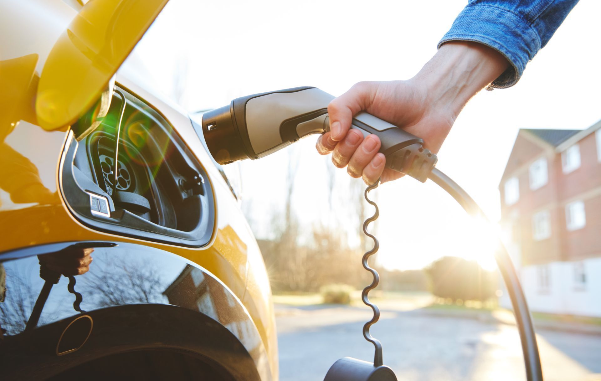 Person plugging an electric vehicle charger into a yellow car.