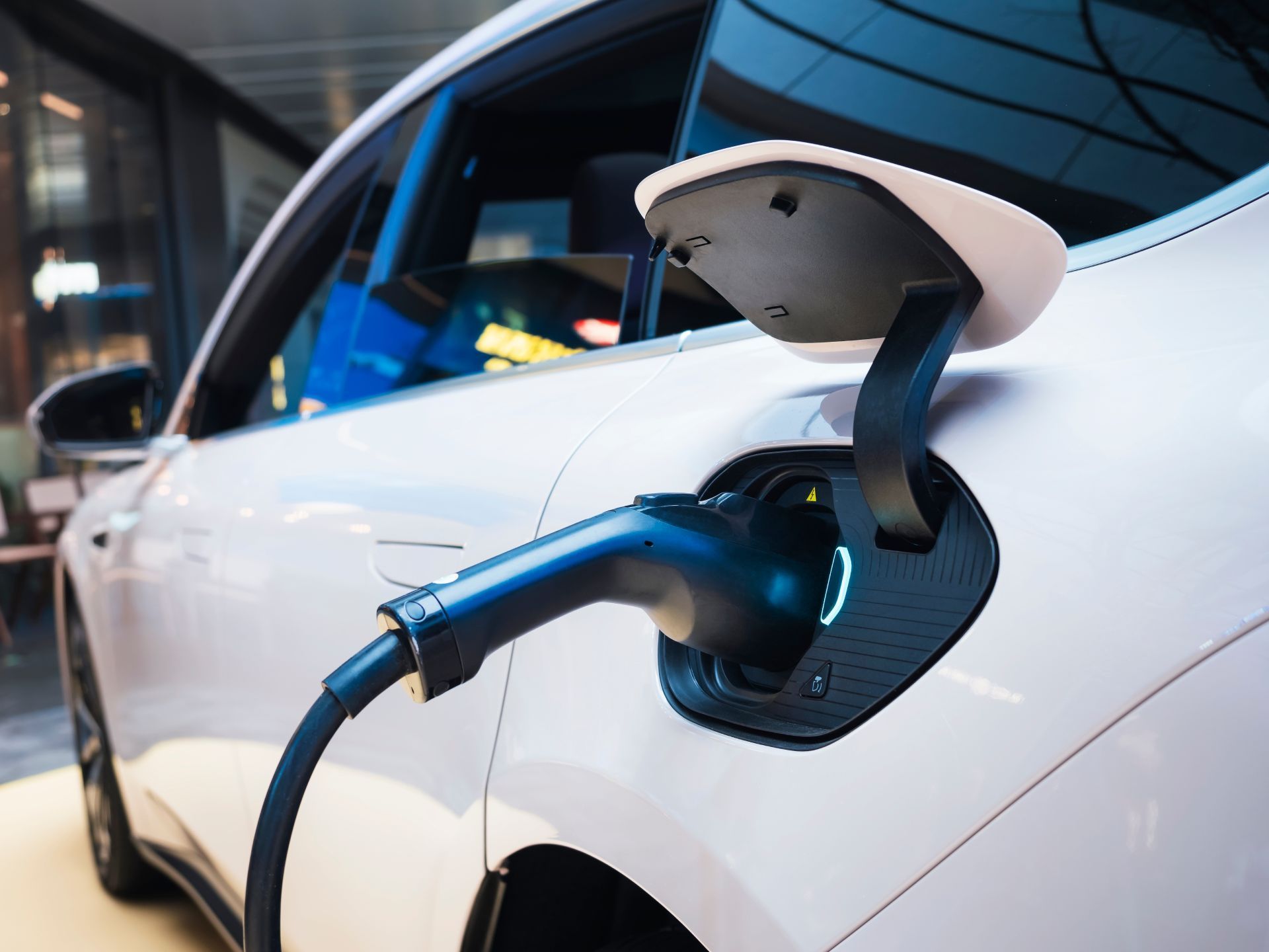 White electric car charging, black charging cable plugged in.