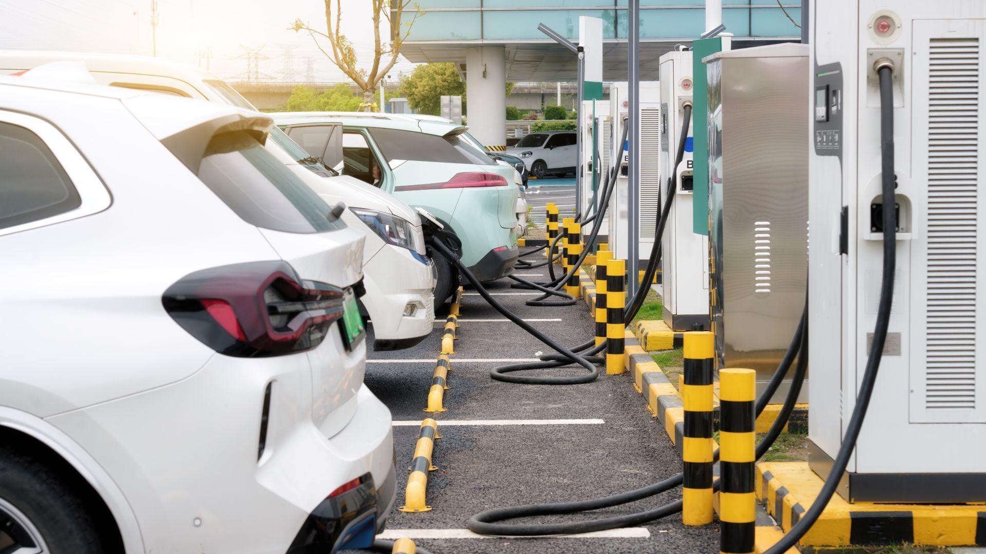 Electric cars charging at a station. White, blue, and light green cars plugged into chargers in an outdoor setting.