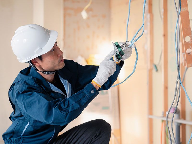 Electrician in a hard hat and gloves working on wiring.