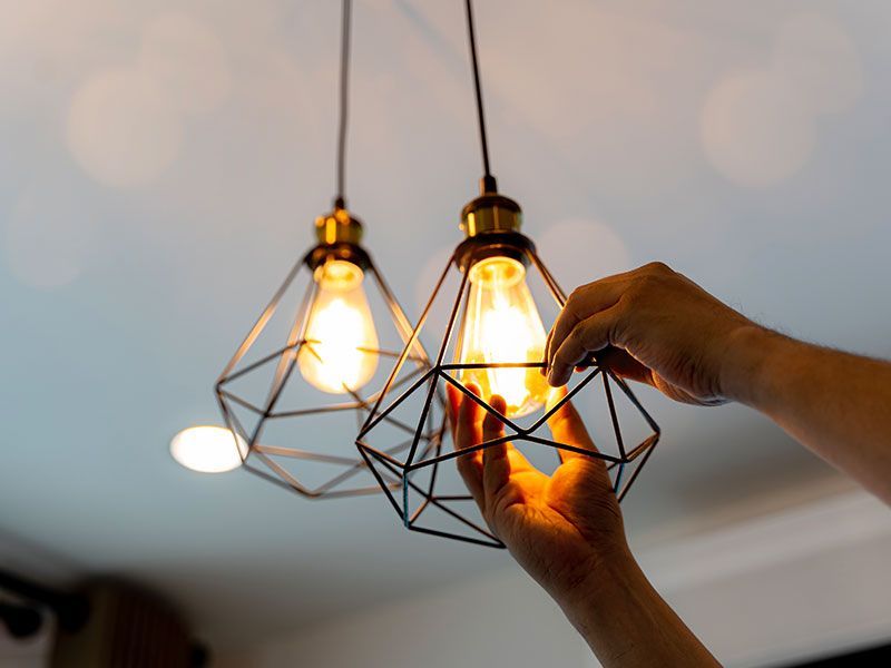 Hands installing a light bulb in a geometric pendant lamp hanging from a white ceiling.
