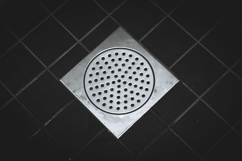 A Square Drain With Holes in It is on a Black Tile Floor — Accredited Plumbing in Kings Point, NSW