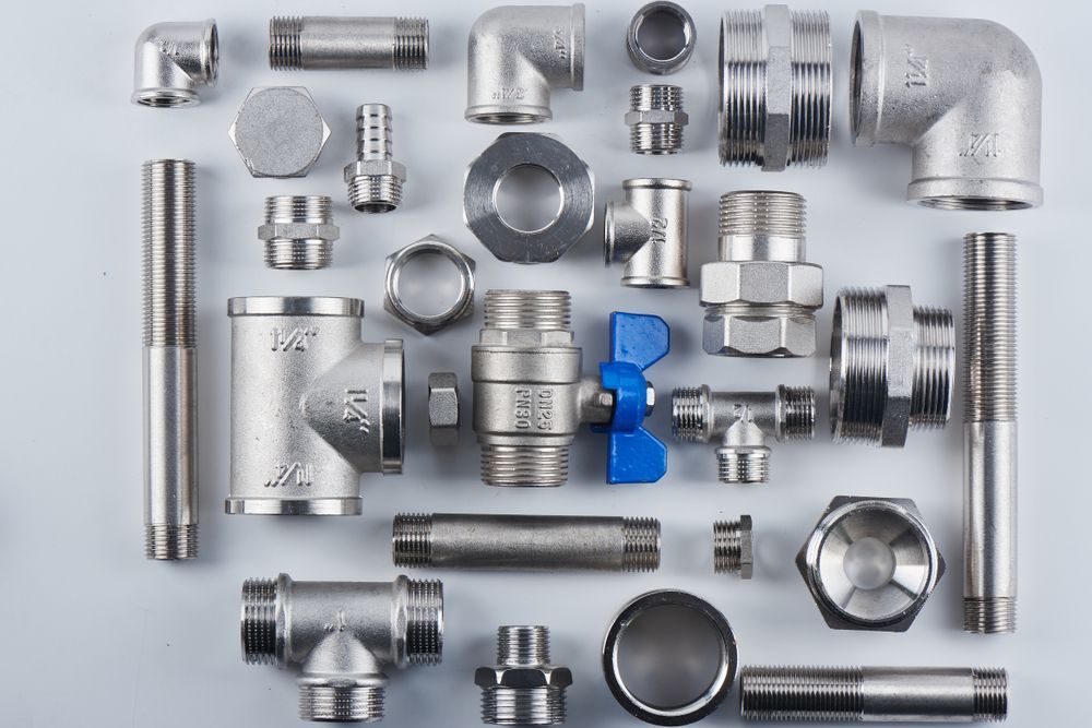 A Bunch of Stainless Steel Pipes and Fittings on a White Surface — Accredited Plumbing in Sussex Inlet, NSW