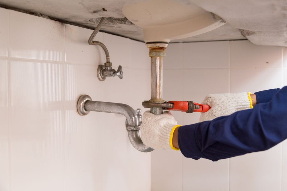 A Plumber is Fixing a Sink Pipe With a Wrench — Accredited Plumbing in Ulladulla, NSW