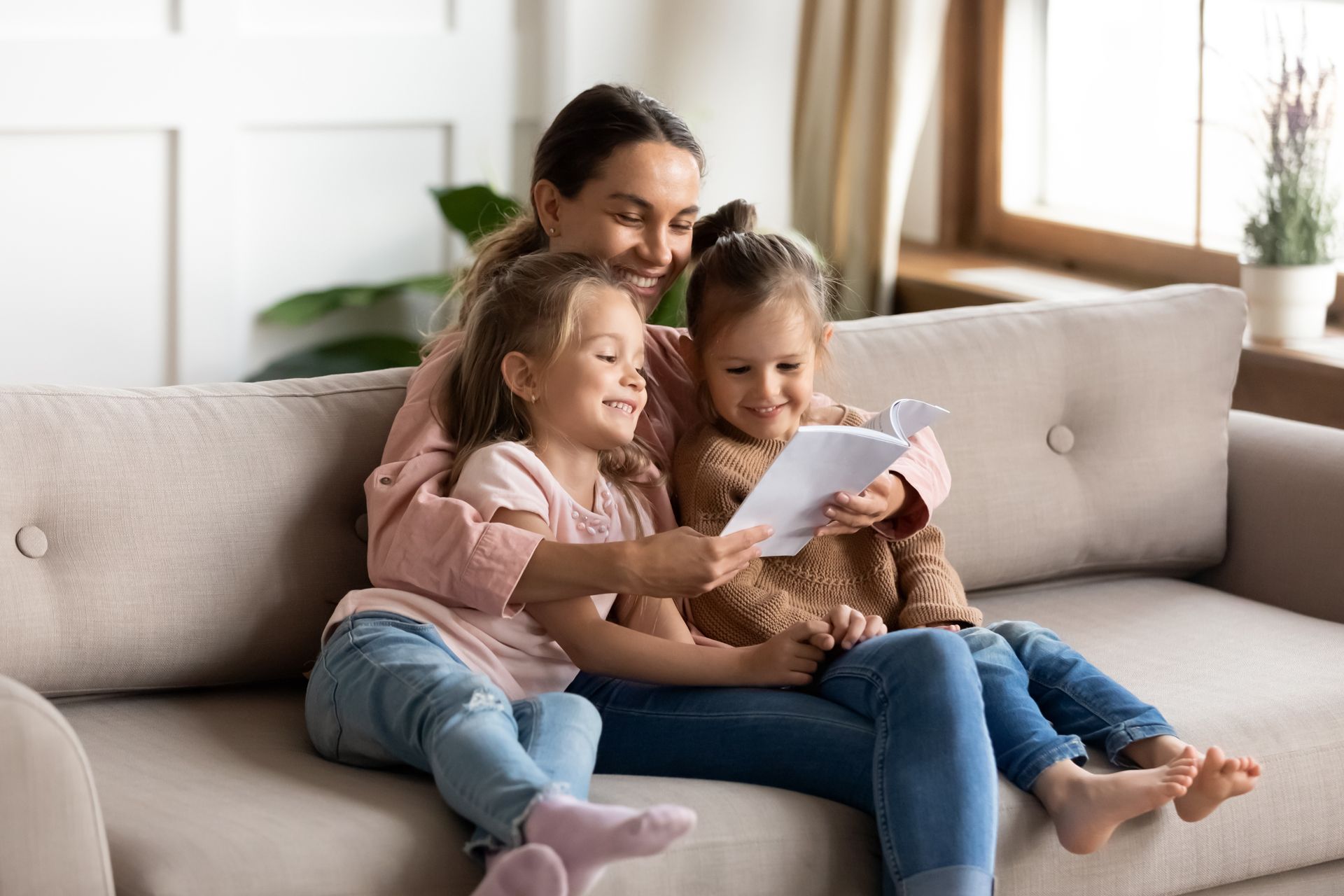 A Woman and Two Little Girls Are Sitting on a Couch Reading a Book