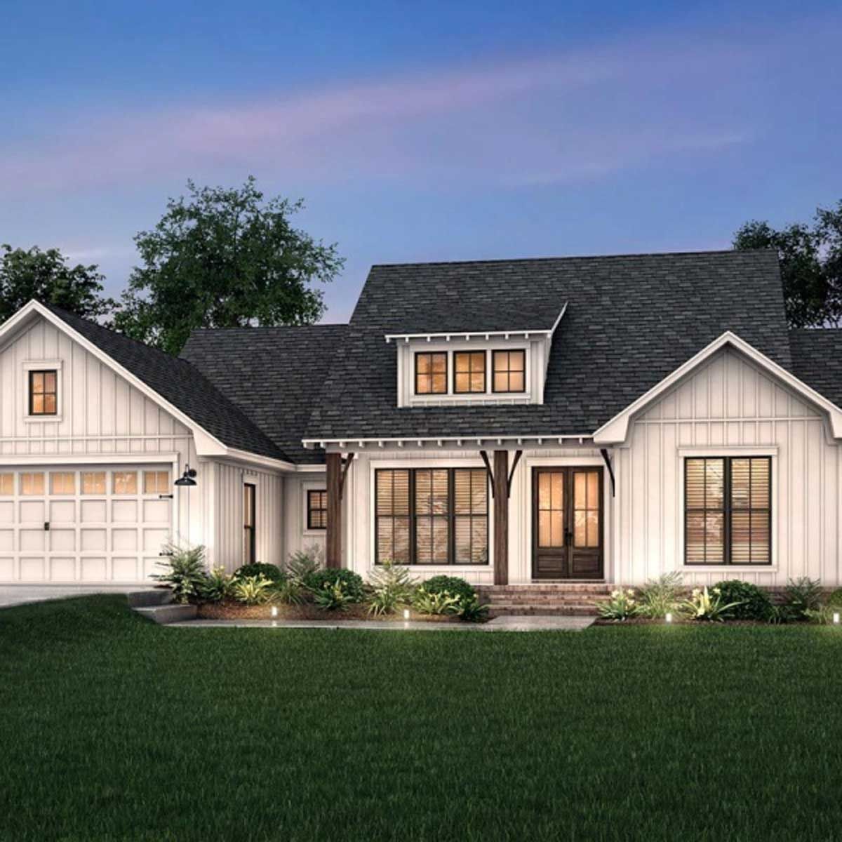 A white house with a black roof is sitting on top of a lush green lawn.