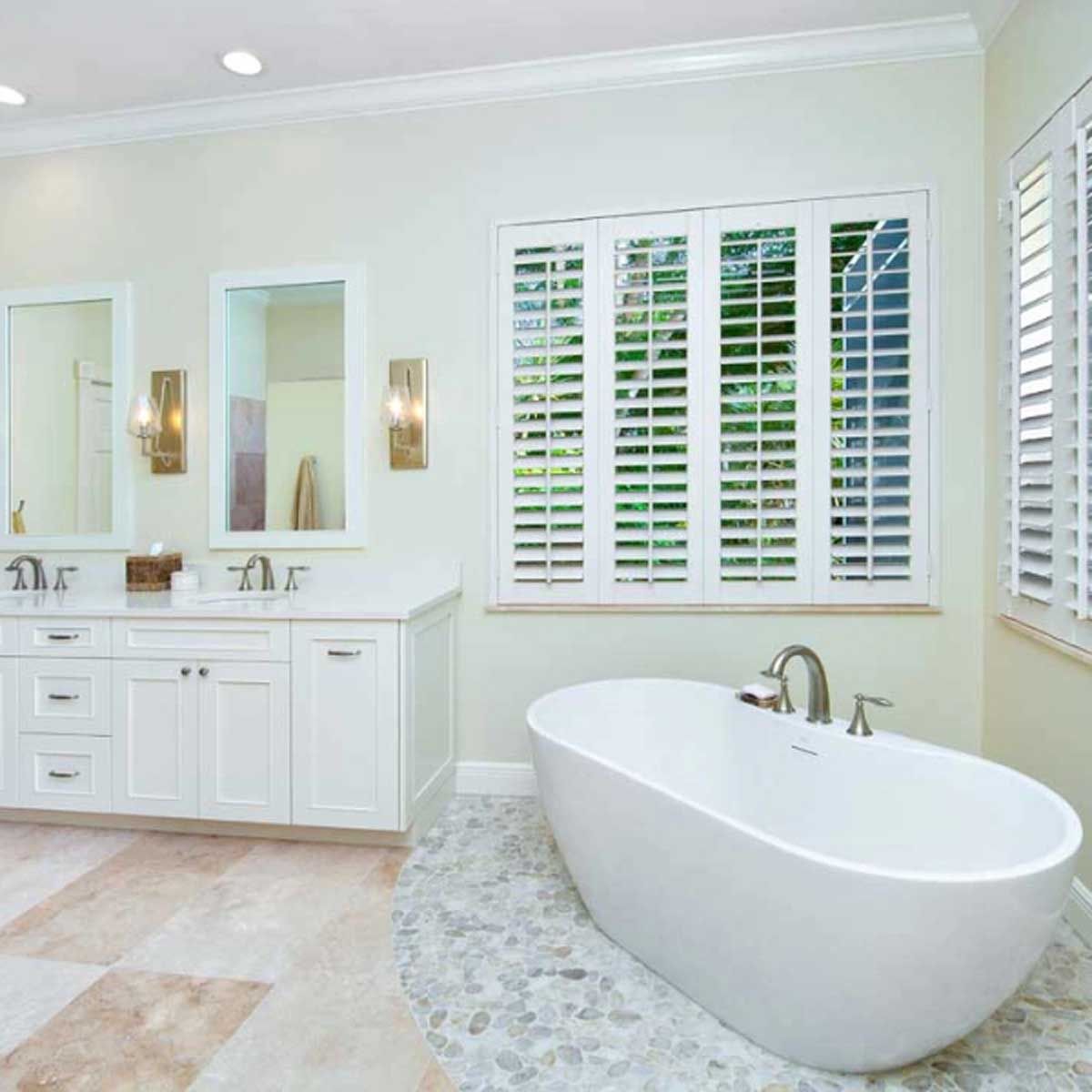 A bathroom with a tub , sink , mirror and shutters