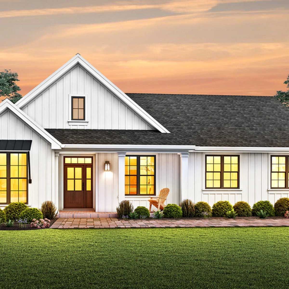 A white house with a black roof is sitting on top of a lush green lawn.