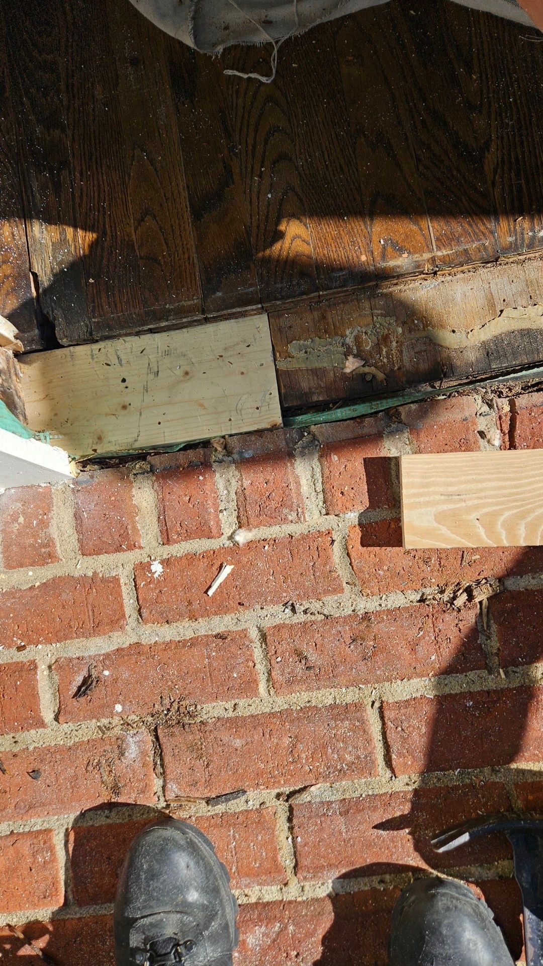 A person is working on a brick wall with a saw and a piece of wood.