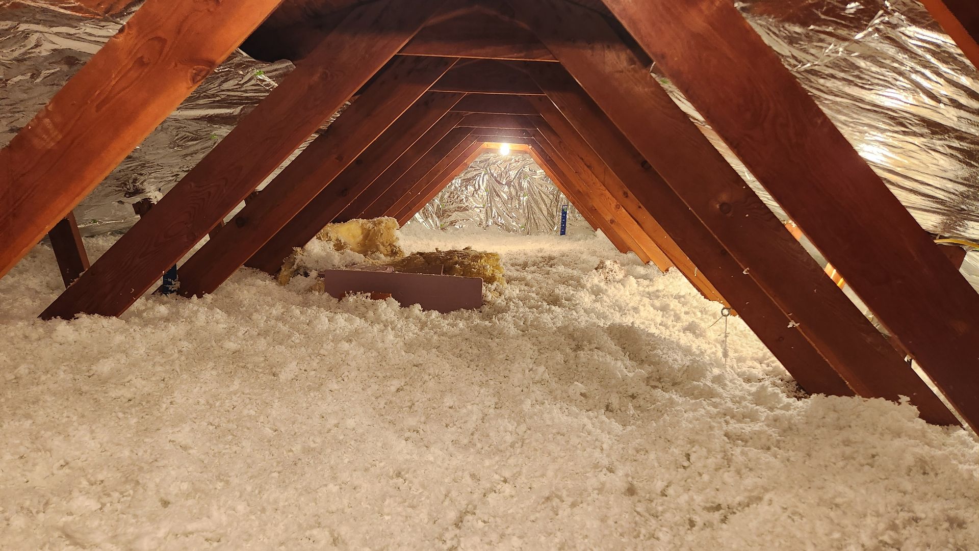 The attic of a house is filled with white insulation and wooden beams.