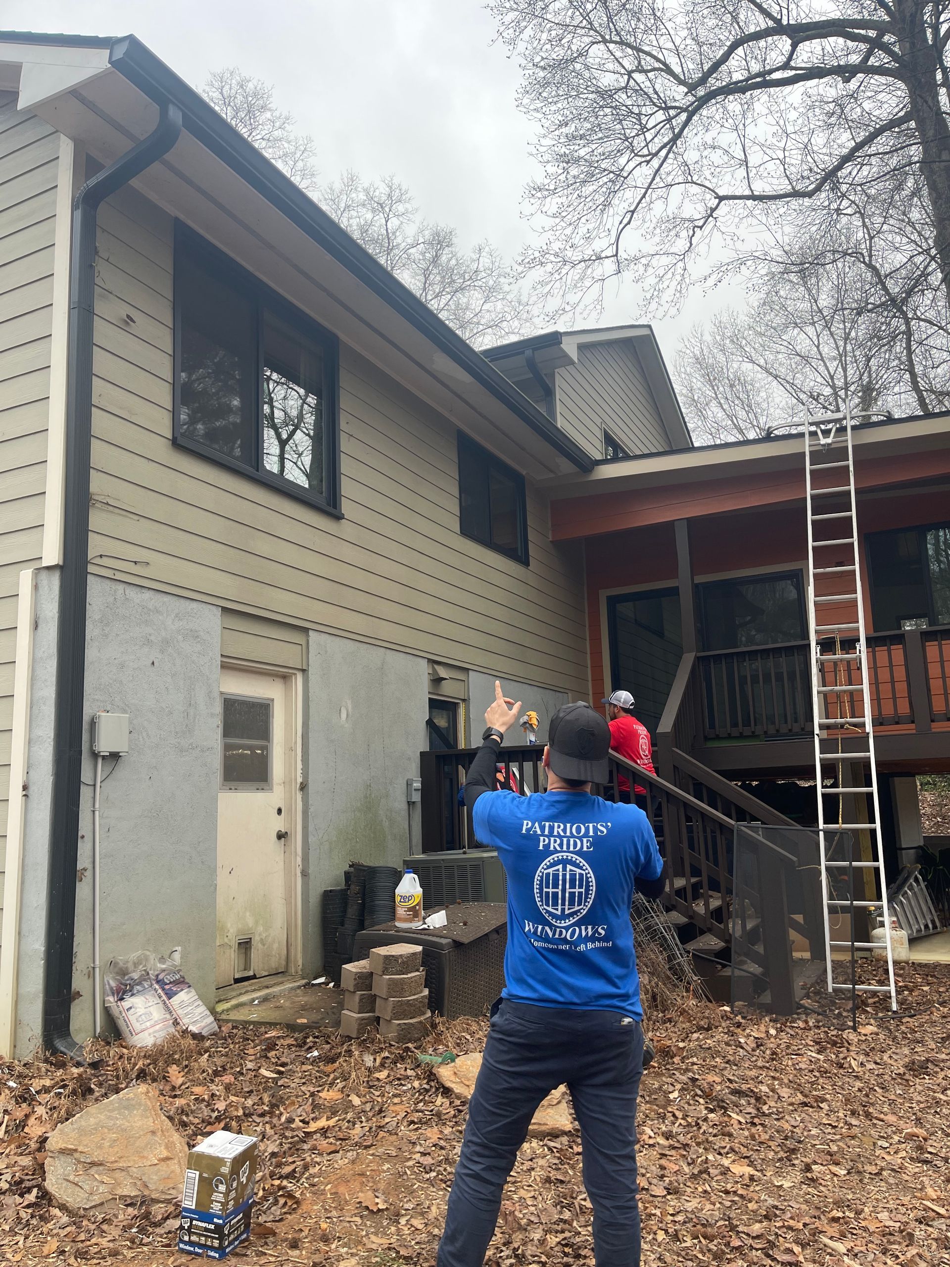 A man in a blue shirt is standing in front of a house.