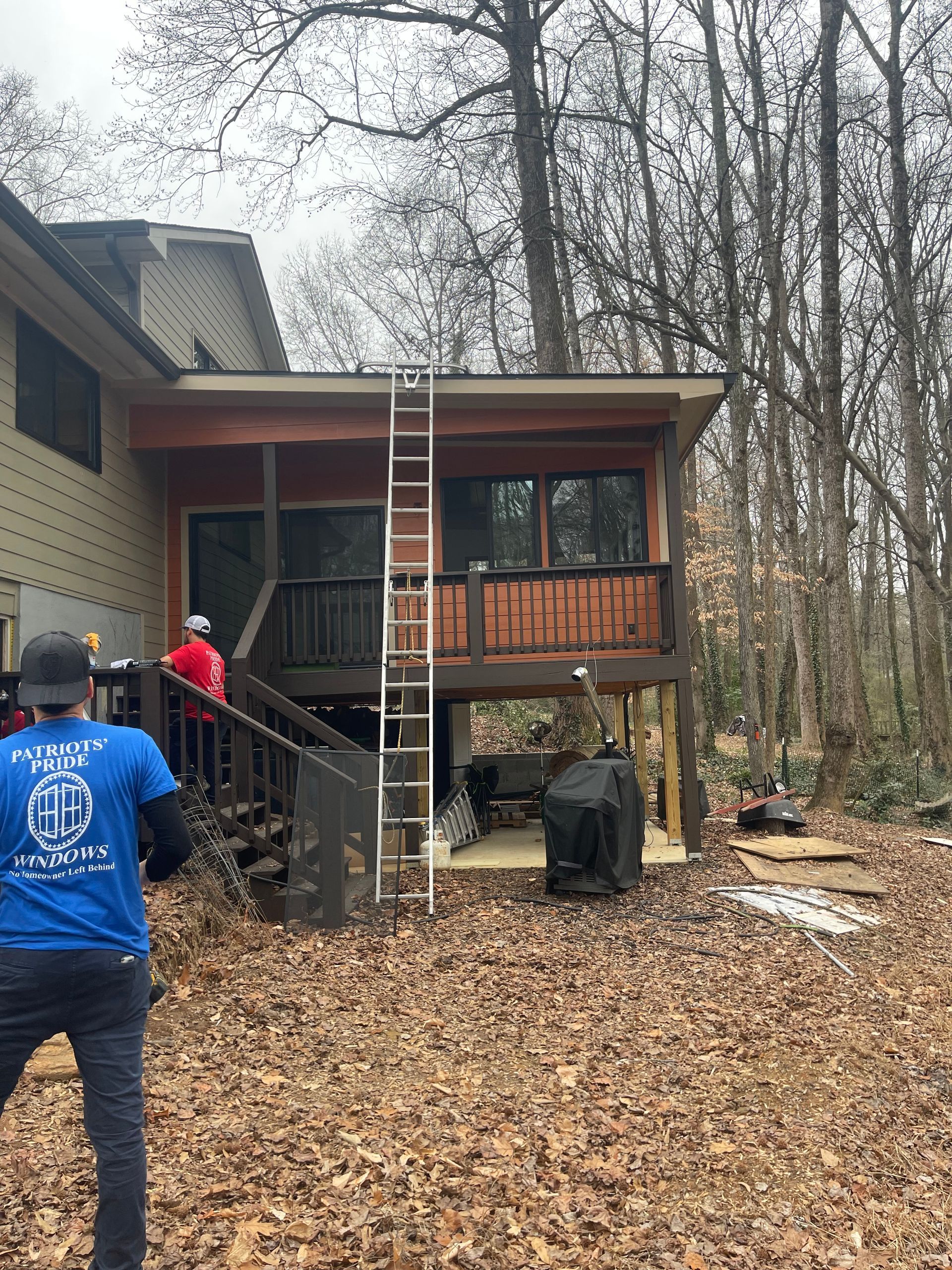 A man in a blue shirt is standing in front of a house with a ladder.