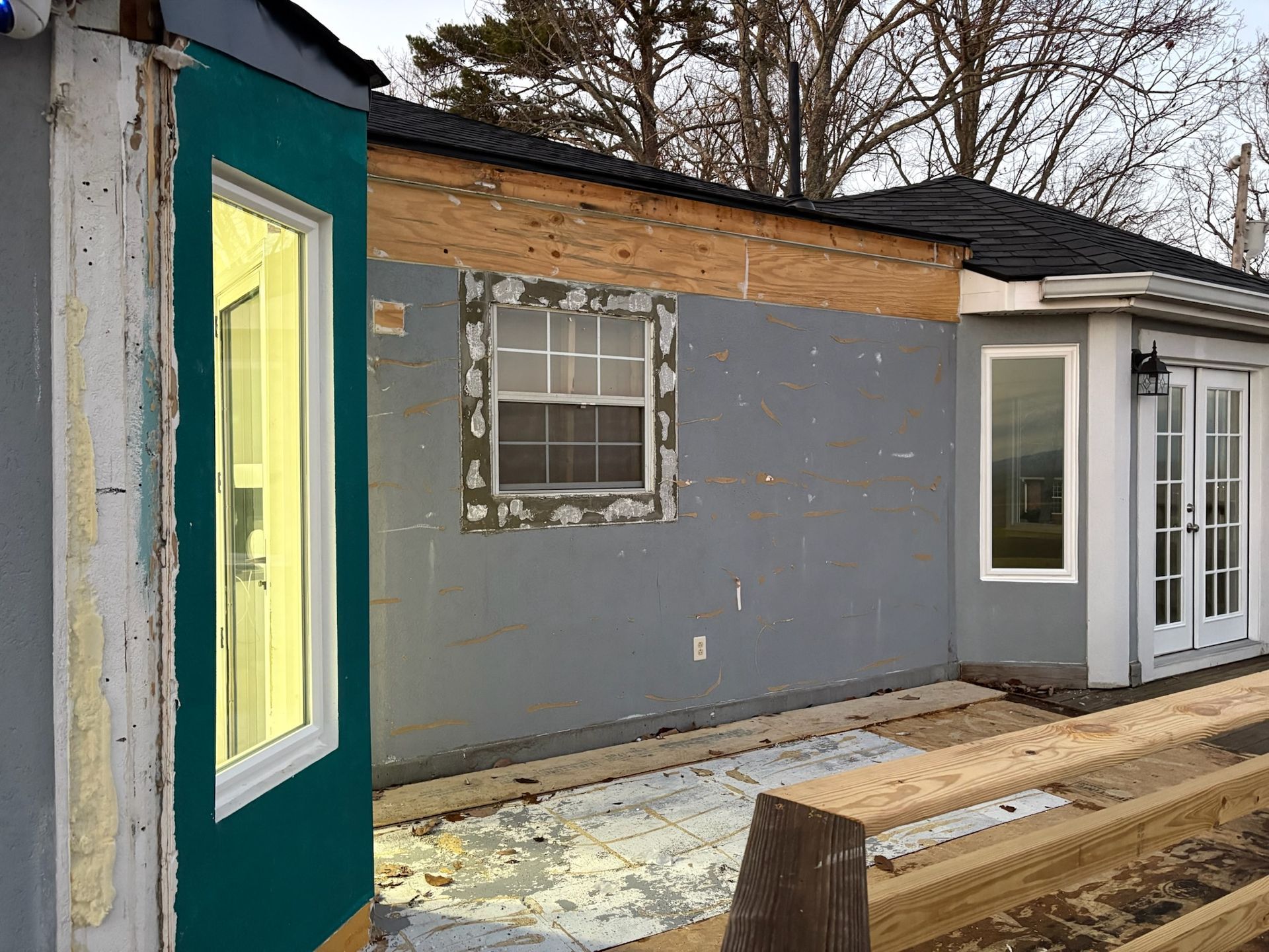 A house is being remodeled with a green door and white windows.