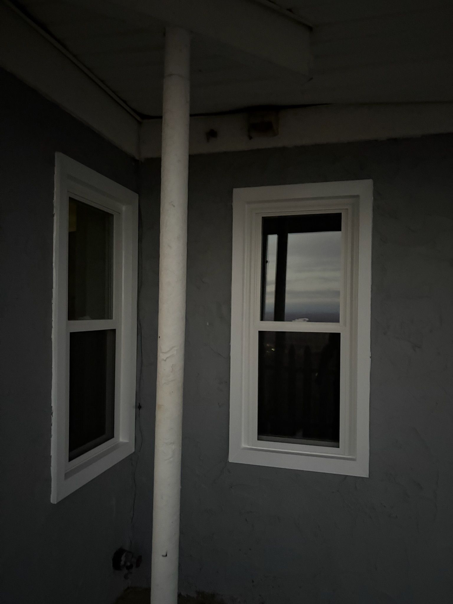 A corner of a house with two windows and a white pipe.