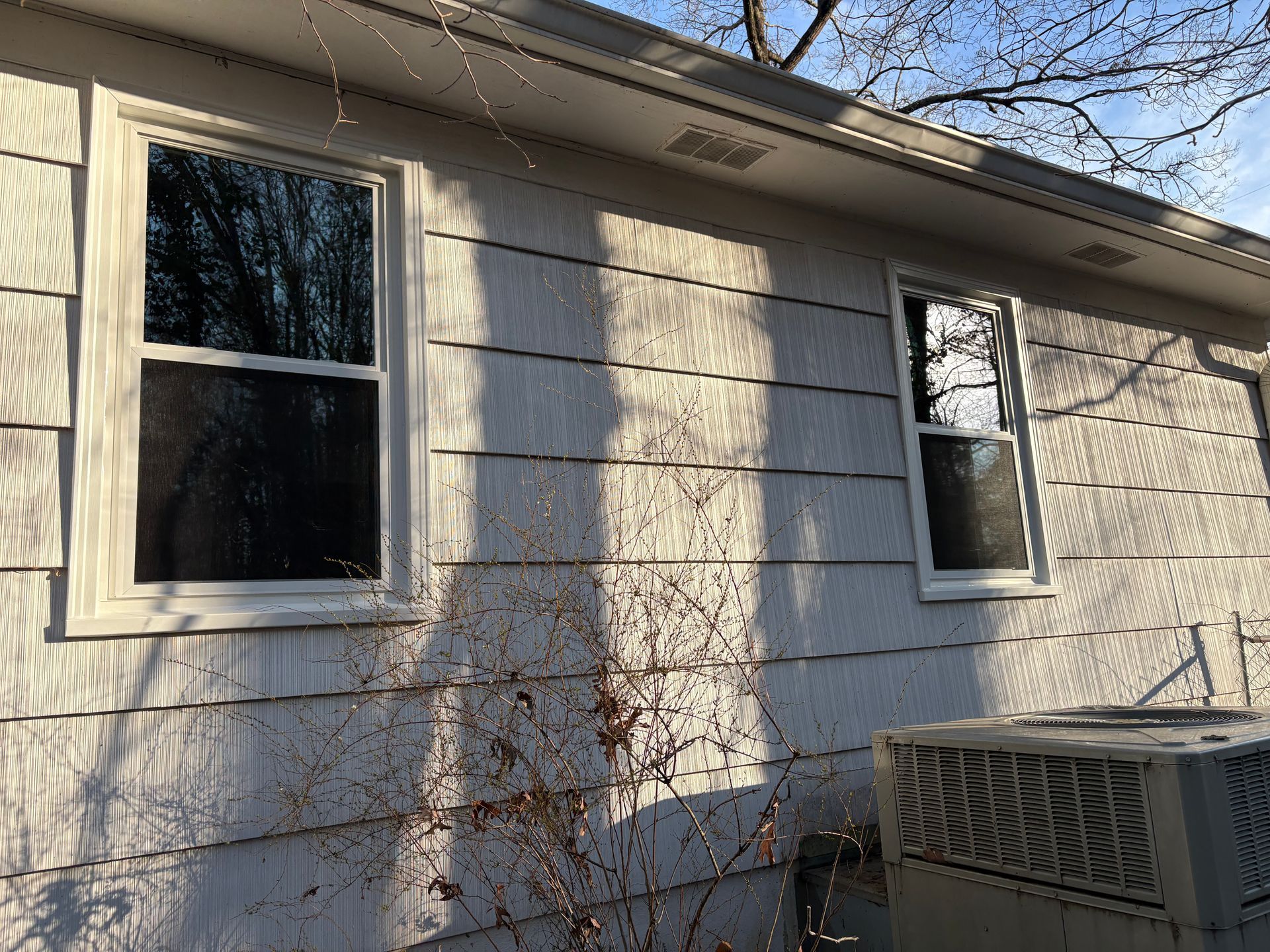 A white house with two windows and an air conditioner on the side.