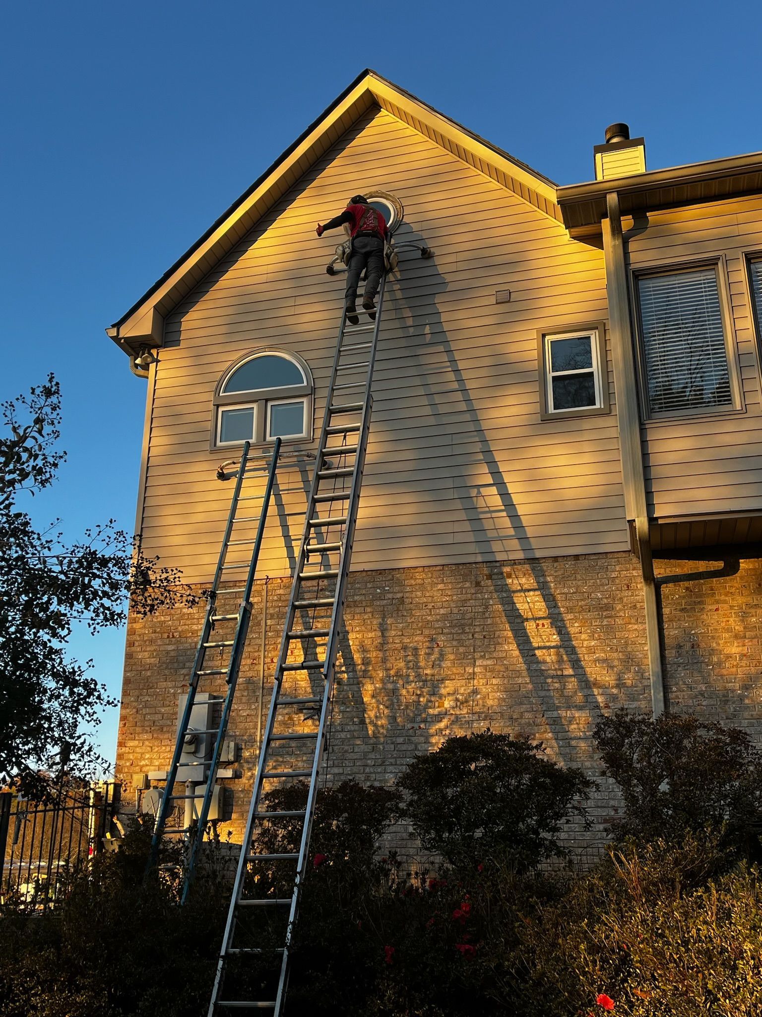 A man on a ladder is working on the side of a house