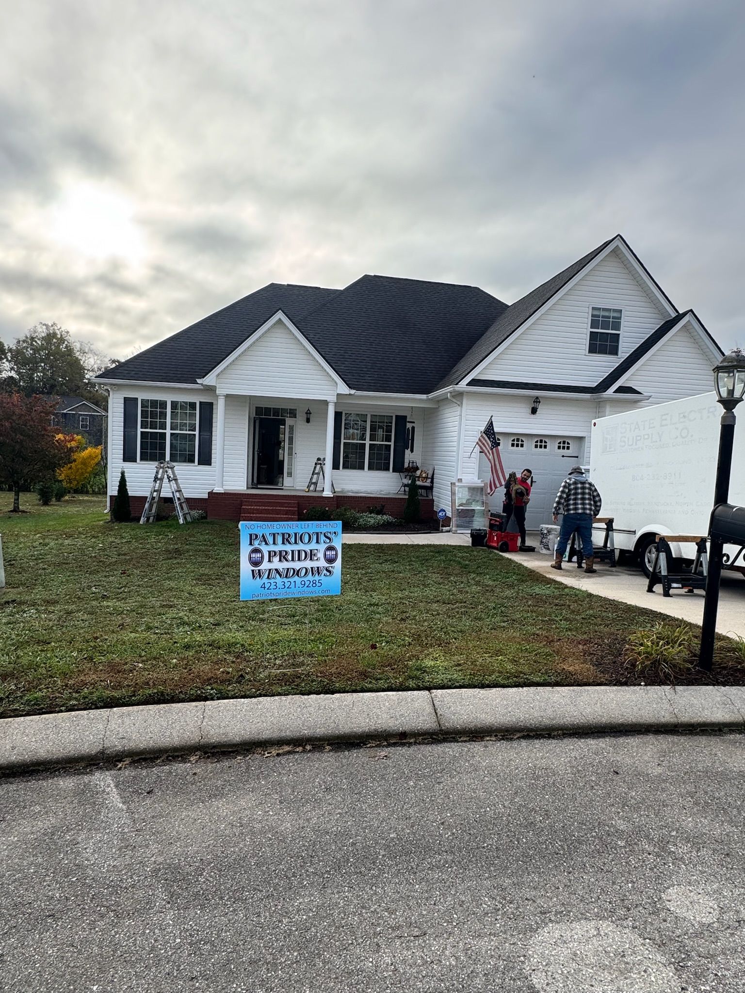A white house with a black roof and a sign in front of it.