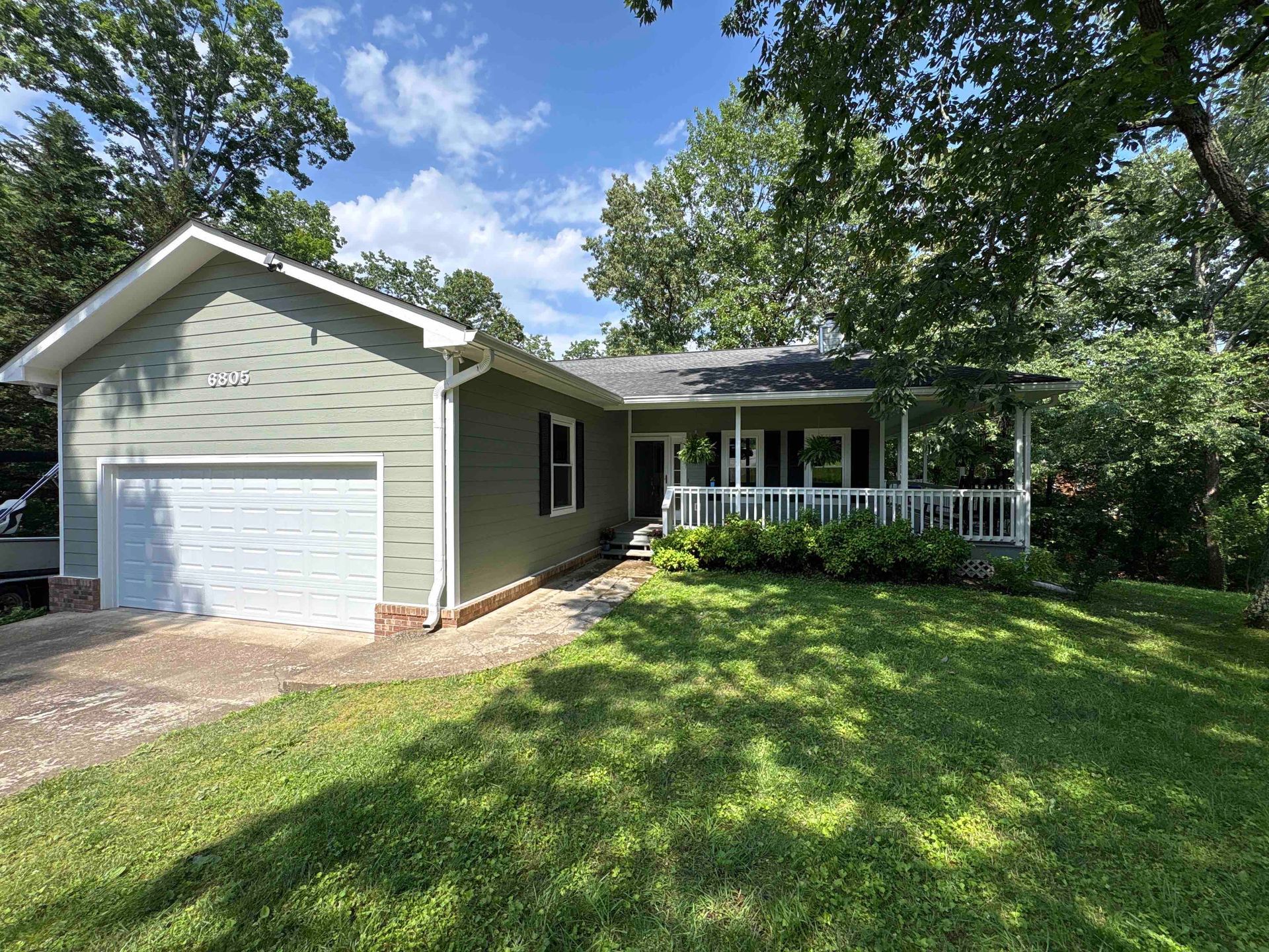 A house with a garage and a porch is sitting on top of a lush green lawn.