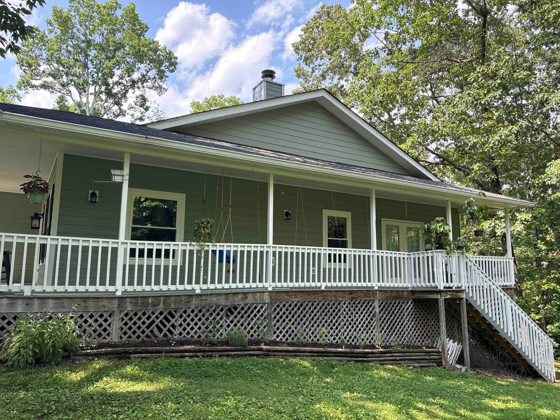 A large green house with a white porch and stairs.