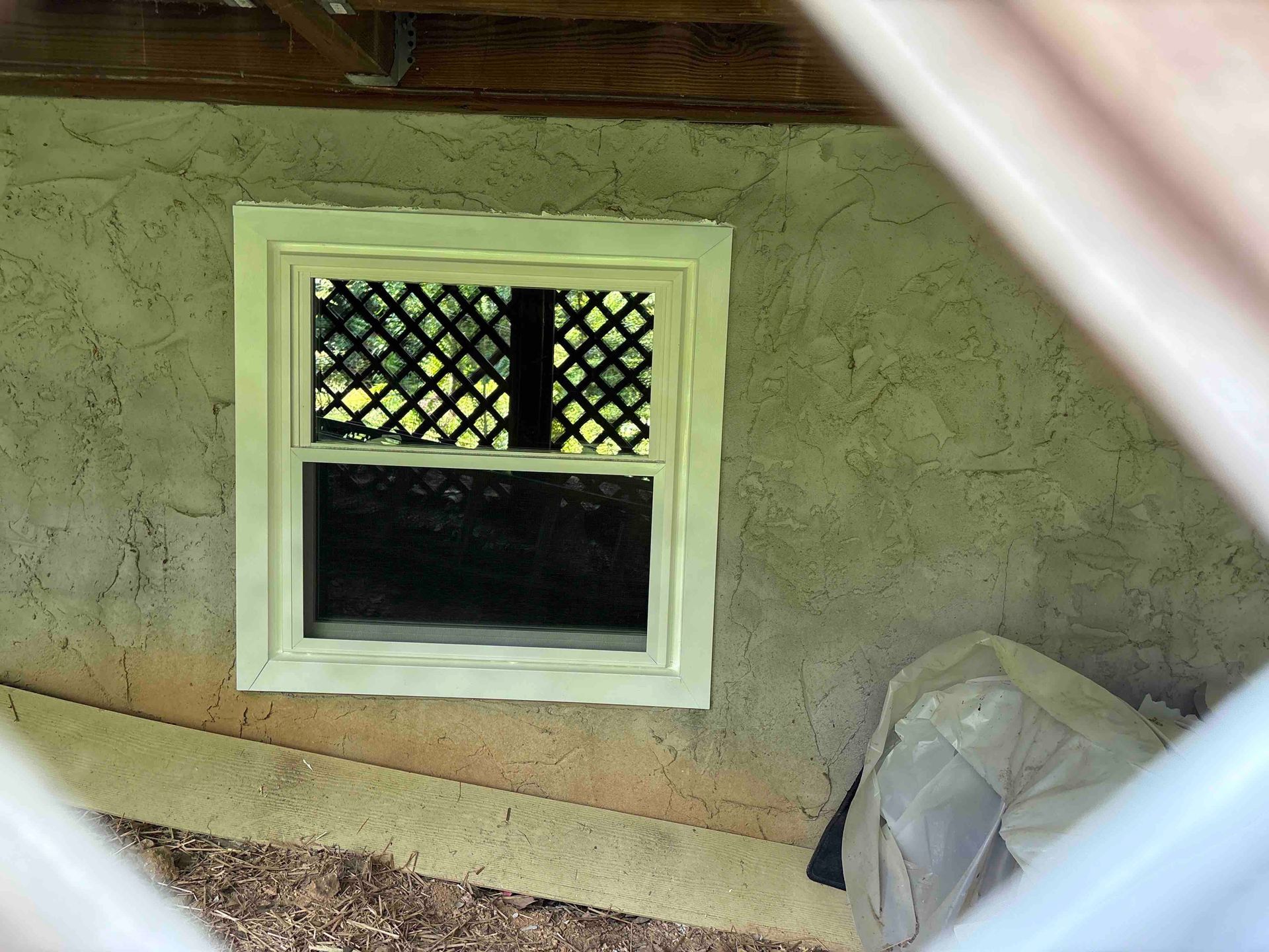 A window with a lattice on it is on the side of a house.