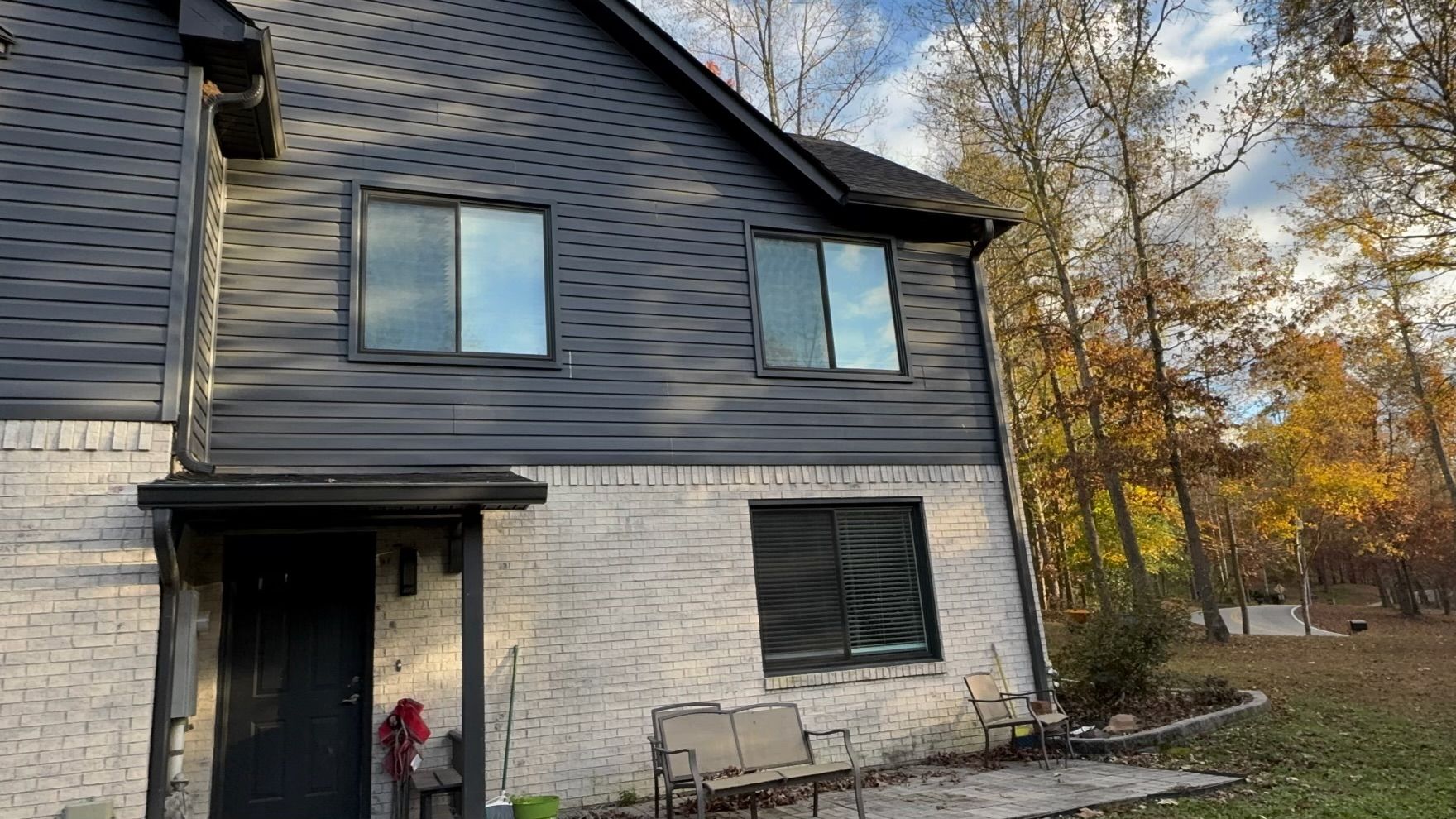 A white brick house with a black siding and a black door is surrounded by trees.