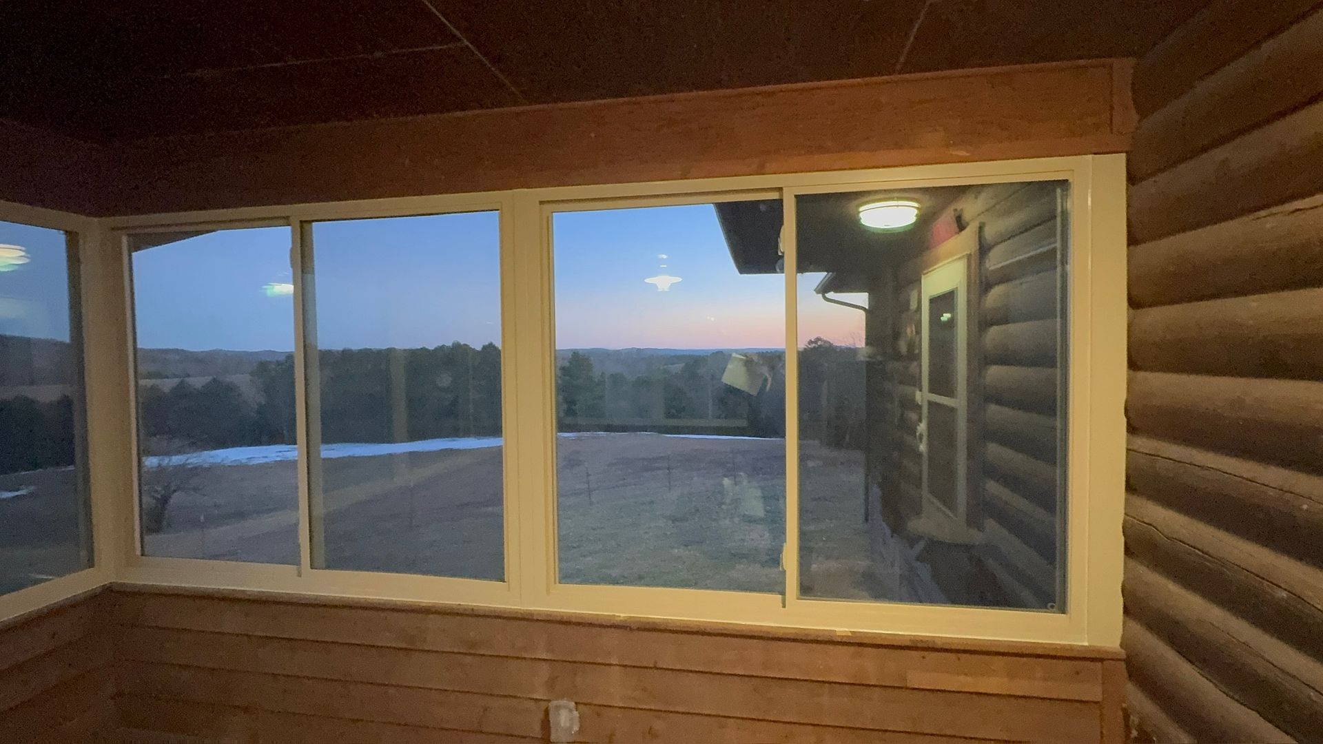 A large window in a log cabin with a view of a sunset.
