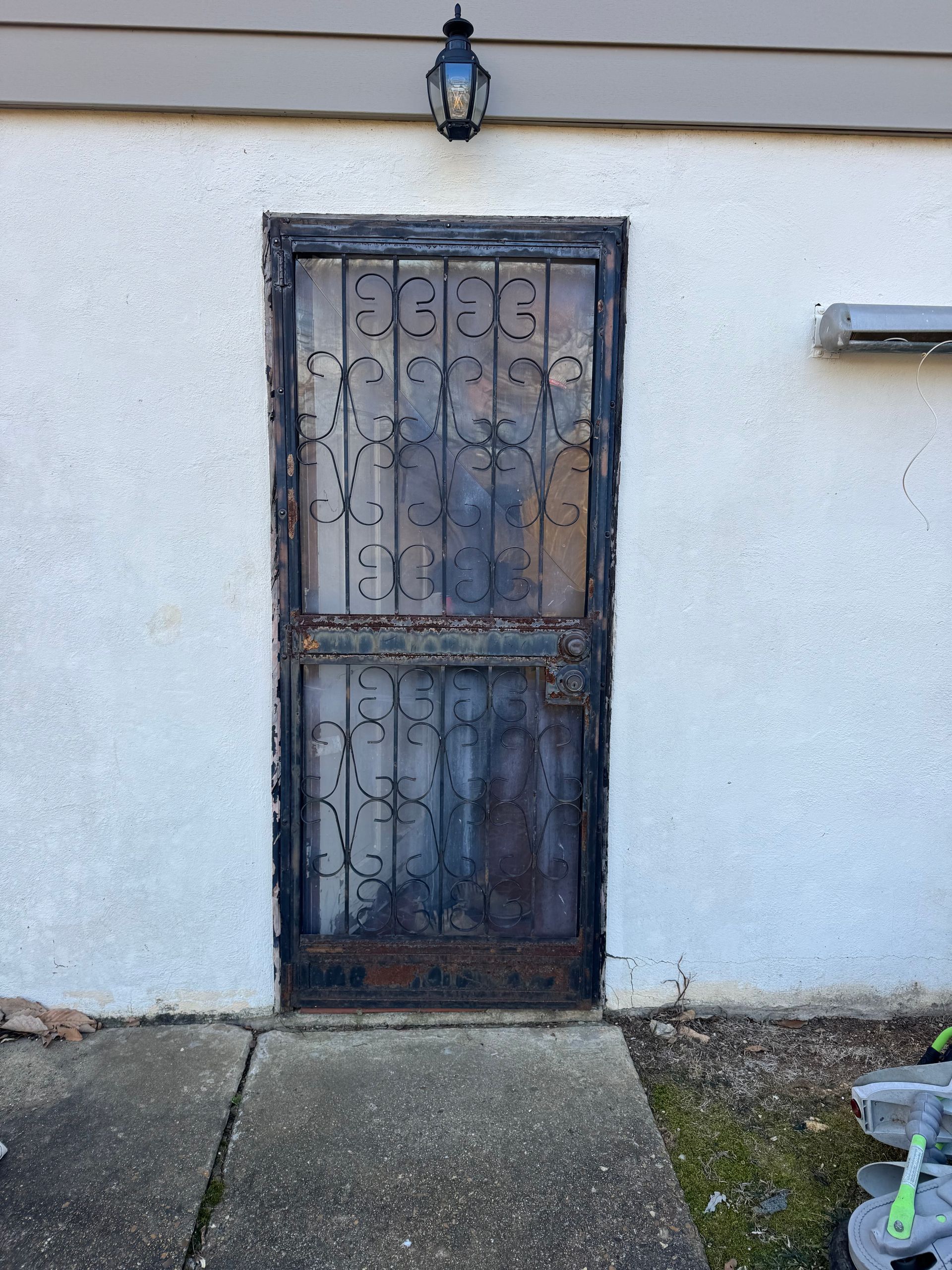 A wrought iron door is sitting on a sidewalk next to a white wall.