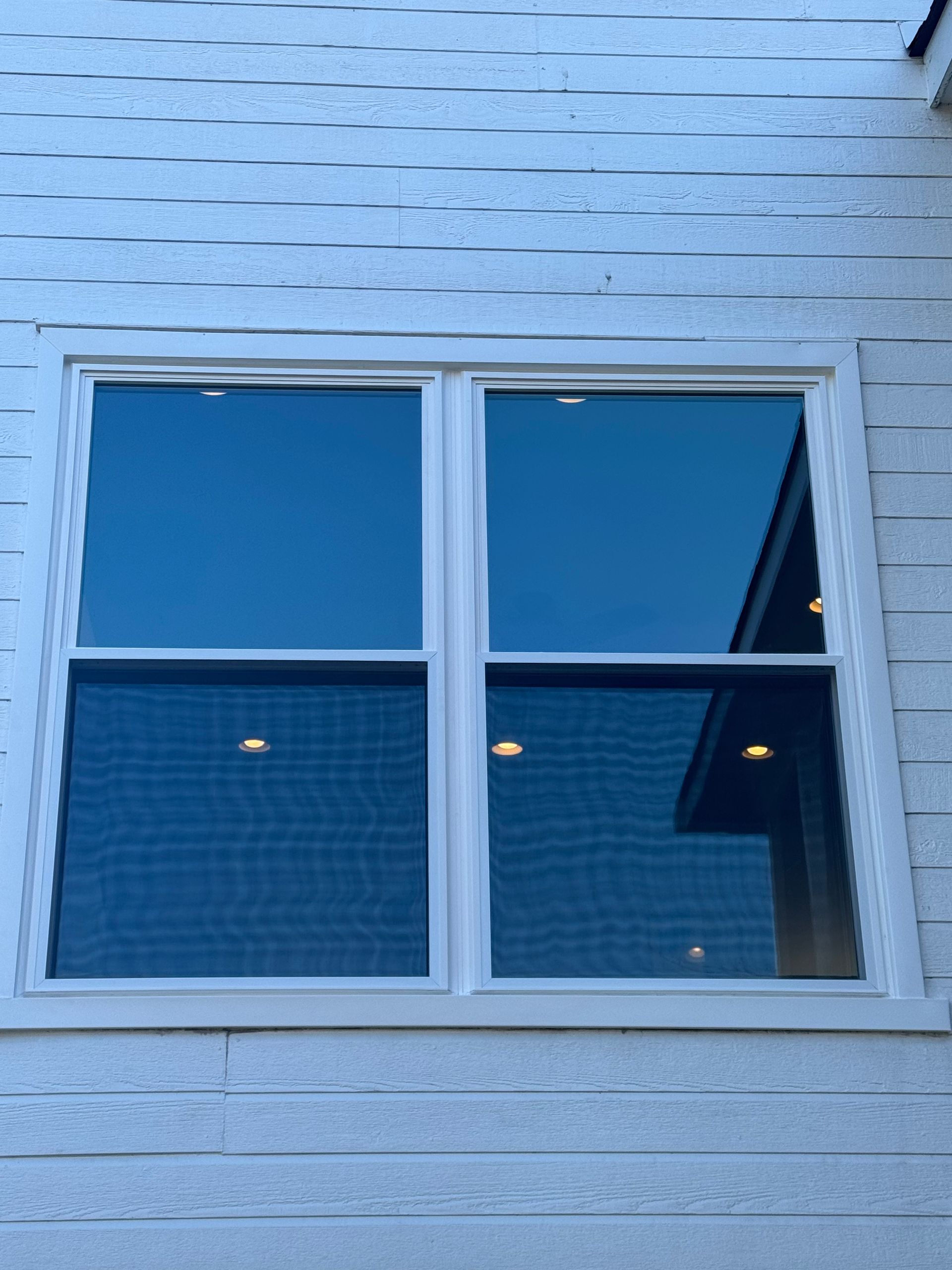 A window on the side of a house with a blue sky reflected in it
