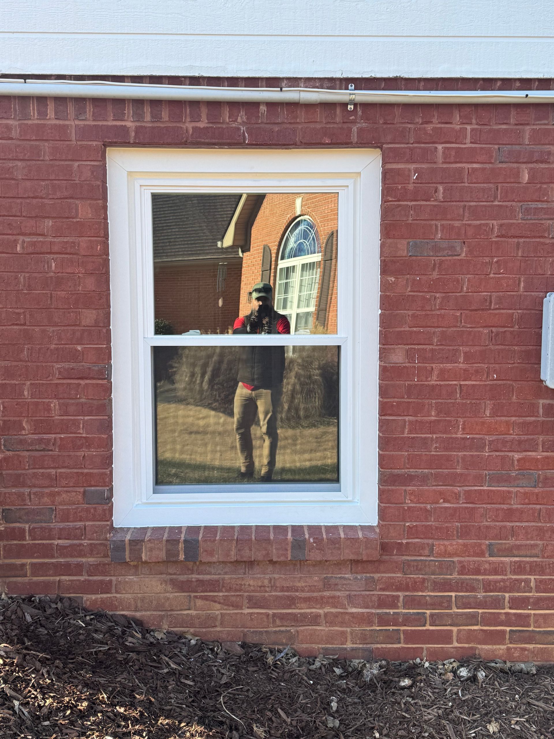 A man is standing in front of a window on a brick building.